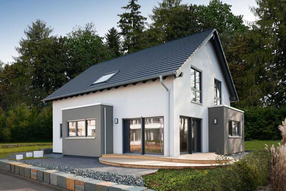 Modernes Musterhaus mit Satteldach und zweifarbiger Putzfassade in Weiß und Grau. Vor dem Haus befindet sich eine Holzterrasse, eingerahmt von Zierkies und einer niedrigen Natursteinmauer.