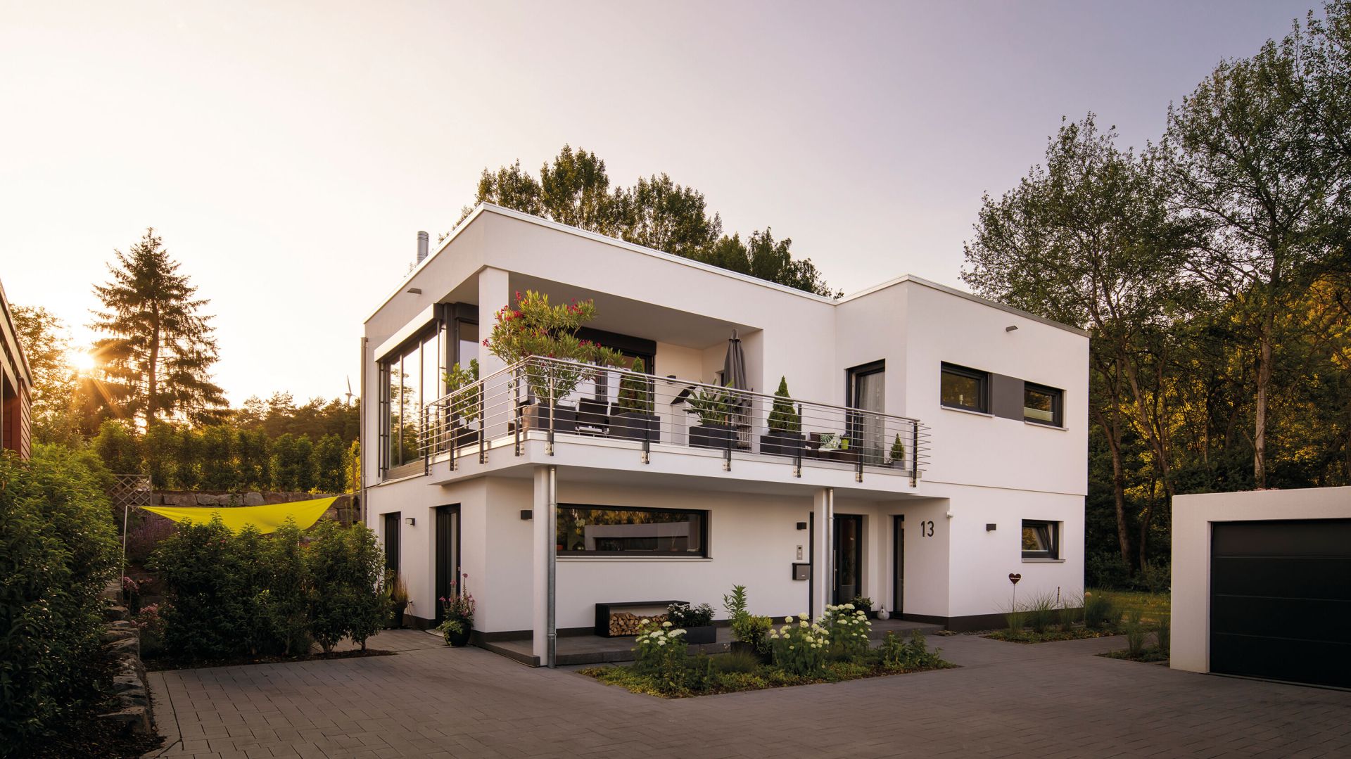 Modernes Flachdachhaus mit klaren Linien, großer Terrasse im Obergeschoss und gepflegtem Garten bei Sonnenuntergang.