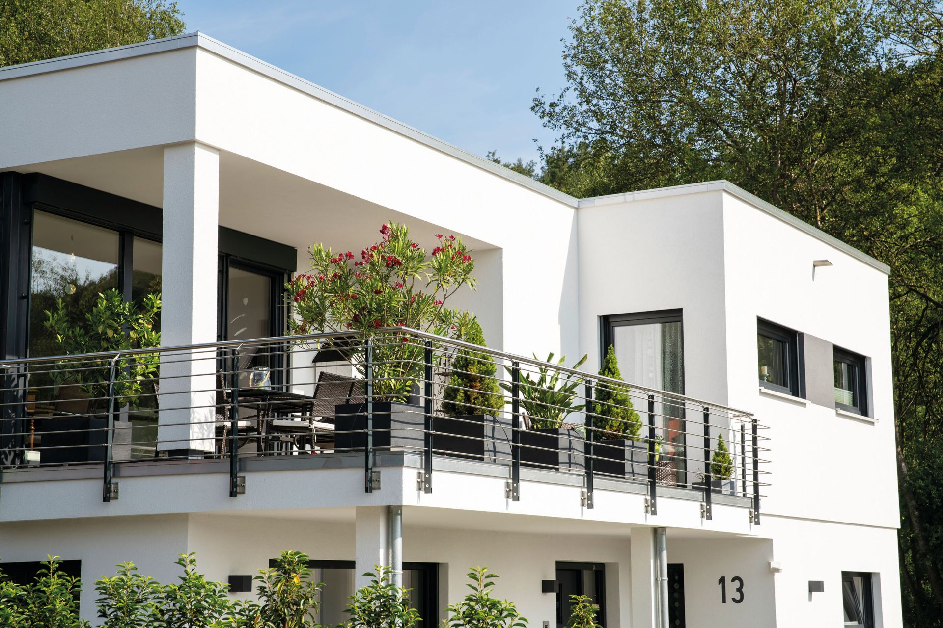 Moderner Balkon eines frei geplanten FingerHauses im Bauhausstil mit Glasgeländer, zahlreichen Pflanzen und Sitzbereich.