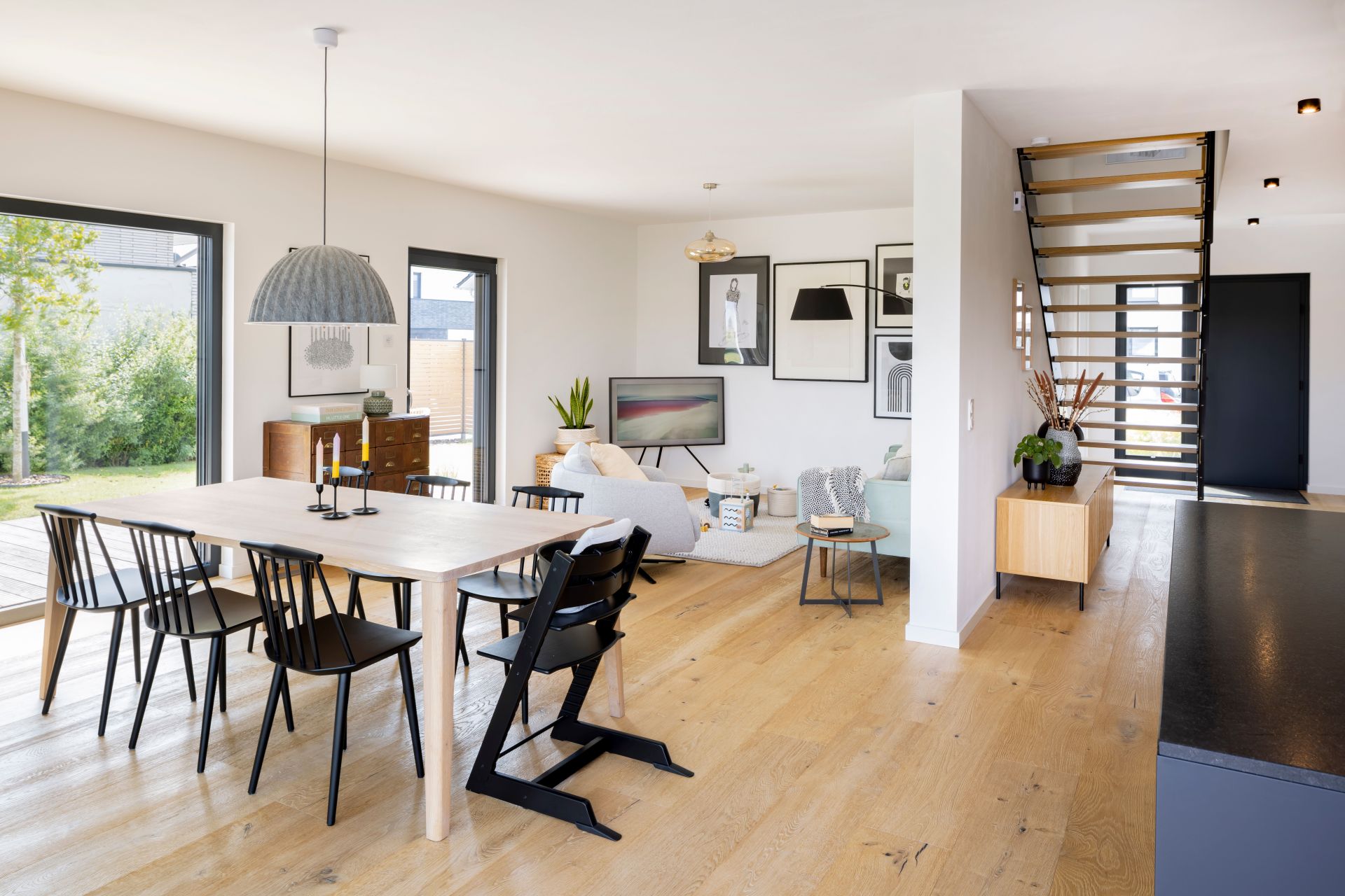 Offener Wohn-, Ess- und Eingangsbereich in einem modernen FingerHaus-Haus mit Holzfußboden, heller Einrichtung und großen Fensterflächen mit Blick in den Garten.