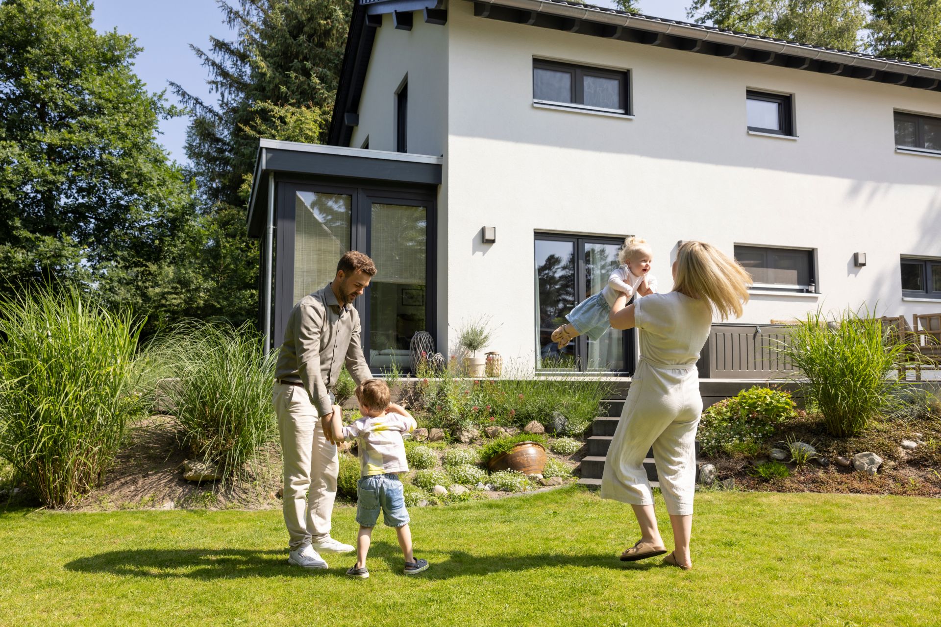 Familie spielt fröhlich im sonnigen Garten eines frei geplanten FingerHaus – moderne Architektur mit heller Fassade und großer Terrasse im Hintergrund.
