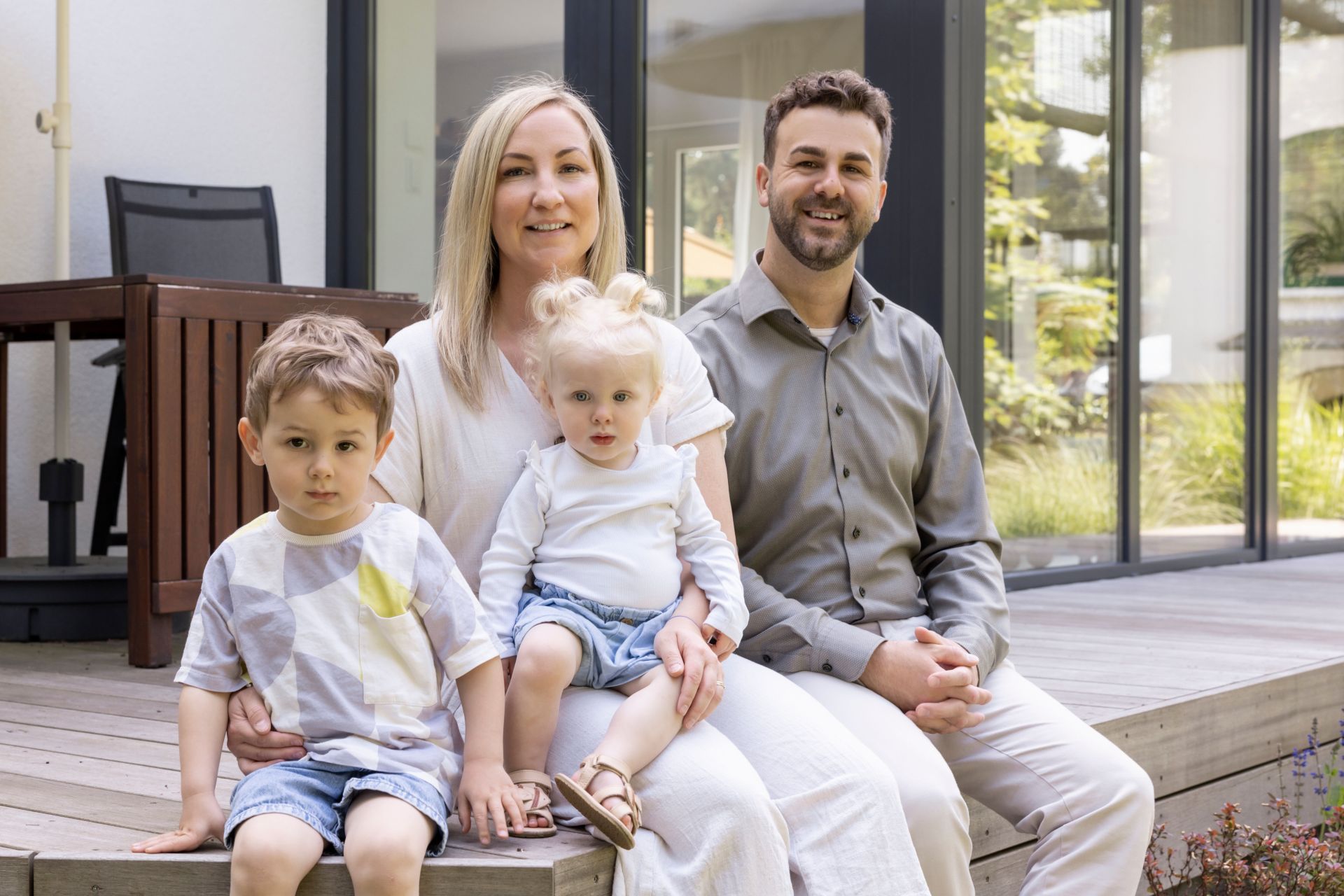 Familie sitzt auf der Terrasse eines frei geplanten FingerHauses und genießt den Sommer.
