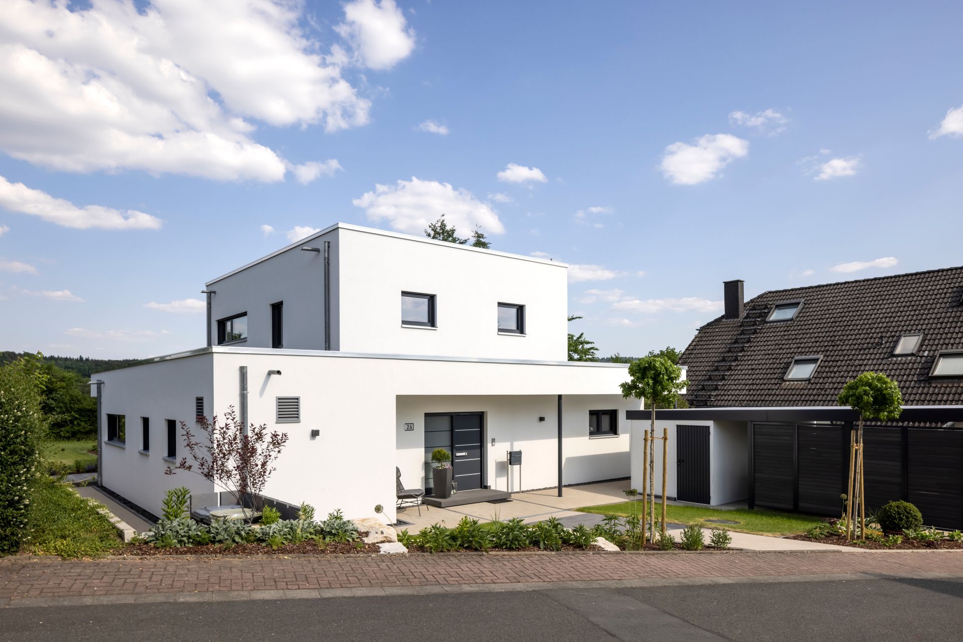 Modernes Einfamilienhaus mit Flachdach, weißer Putzfassade und überdachtem Eingangsbereich in Hanglage