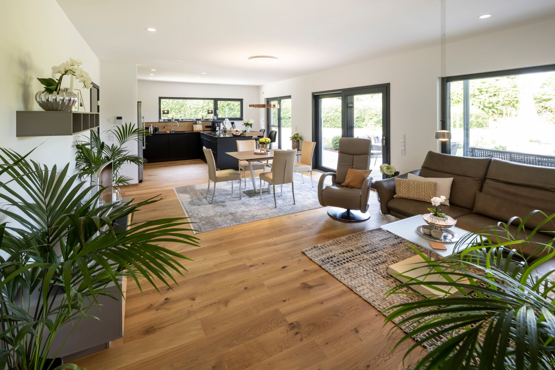 Offener Wohn-, Ess- und Küchenbereich mit viel Tageslicht, modernen Möbeln und warmem Holzfußboden.