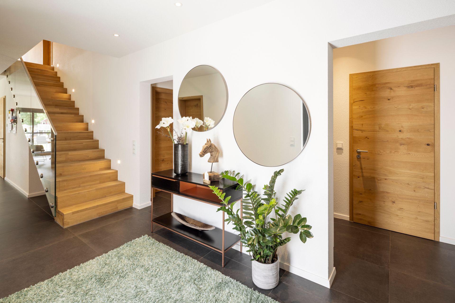 Moderner Eingangsbereich in einem frei geplanten FingerHaus mit Holztreppe, dekorativer Konsole, Spiegeln, Zimmerpflanze und stilvollem Design.
