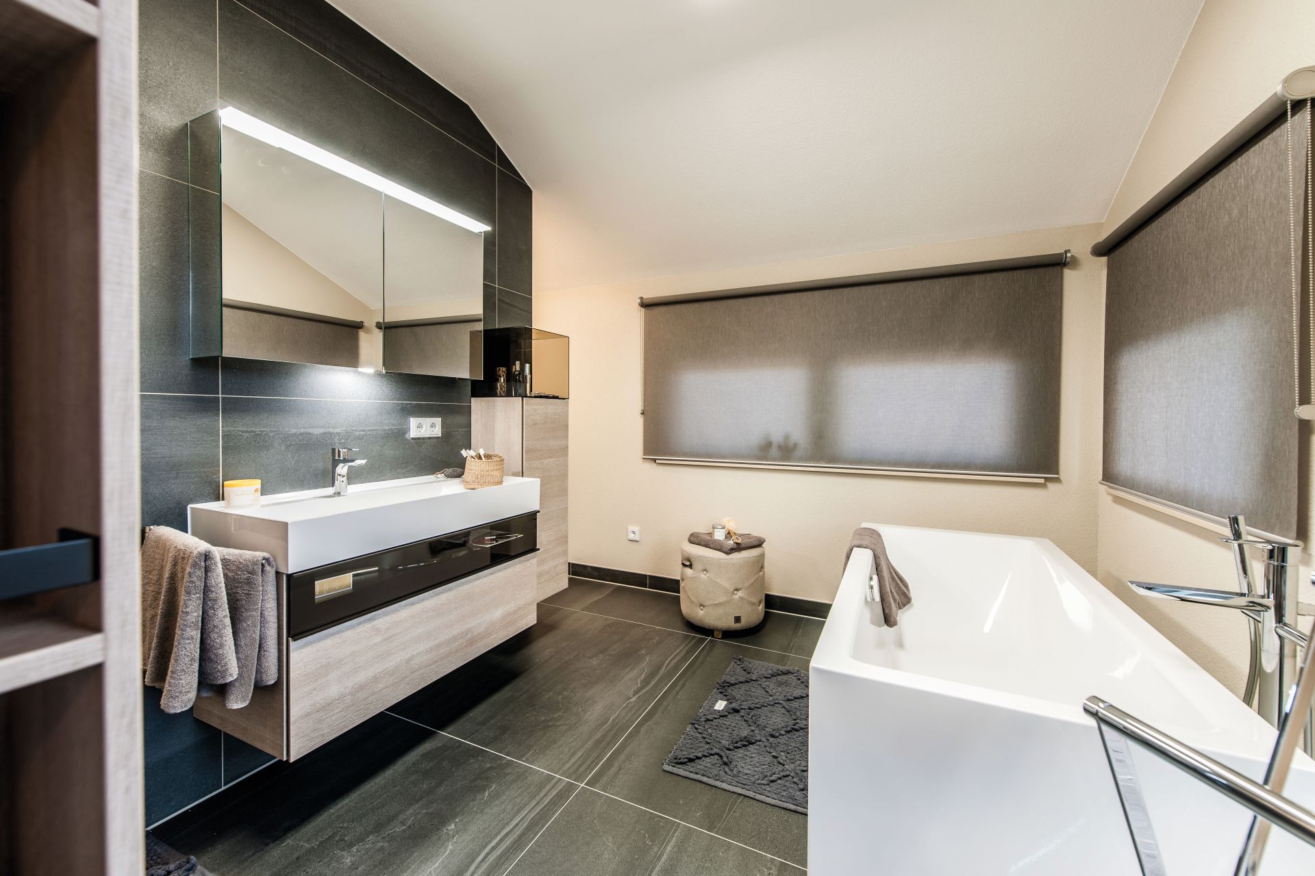 Modernes Badezimmer mit freistehender Badewanne, großem Spiegel über dem Waschbecken und dunklen Bodenfliesen