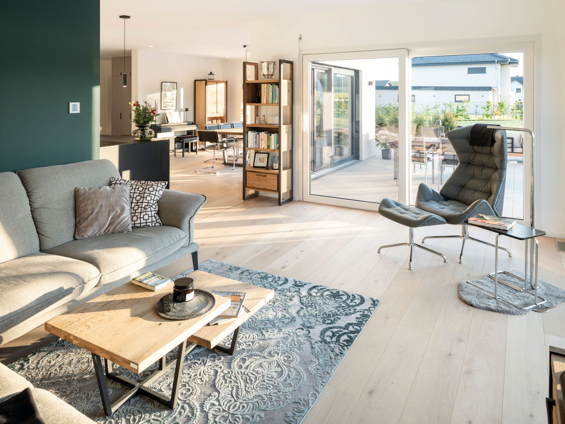 Heller Wohnbereich mit Sofa, Couchtisch, Sessel, Bücherregal und großer Glasfront zur Terrasse.
