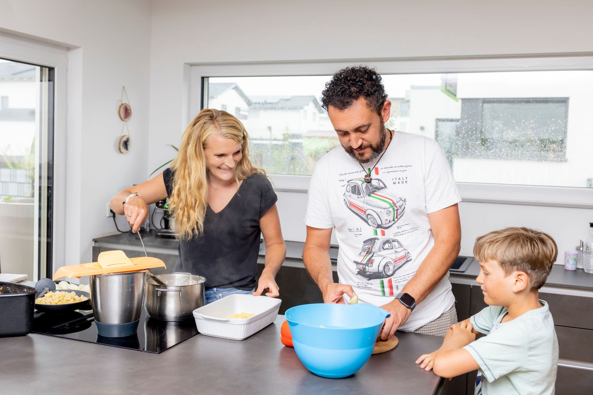 Zwei Erwachsene und ein Kind bereiten gemeinsam Essen an einer Kücheninsel zu.