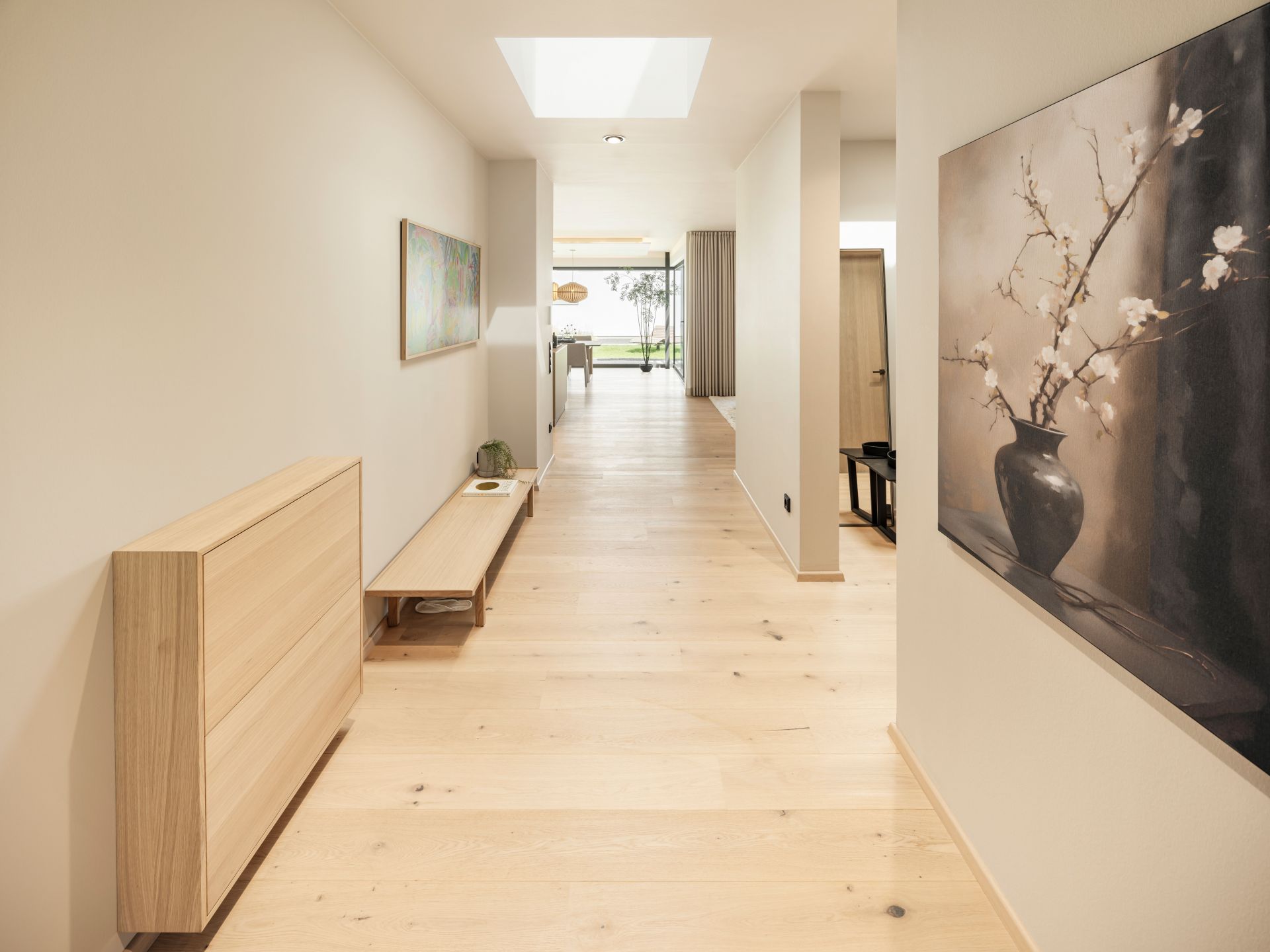Langer Flur im FingerHaus Musterhaus NIVO in Frankenberg mit Holzboden, Sitzbank, Wandbildern und Oberlicht.