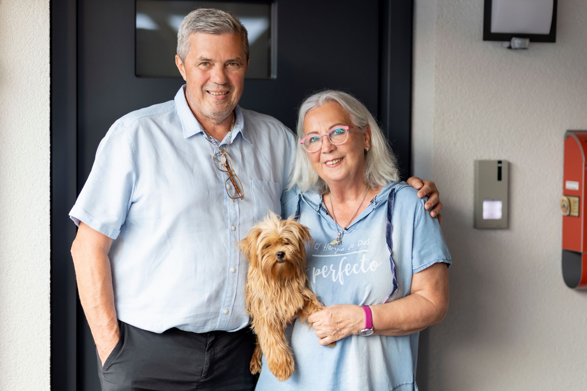 Älteres Paar mit kleinem Hund vor dem Hauseingang eines modernen Flachdachhauses