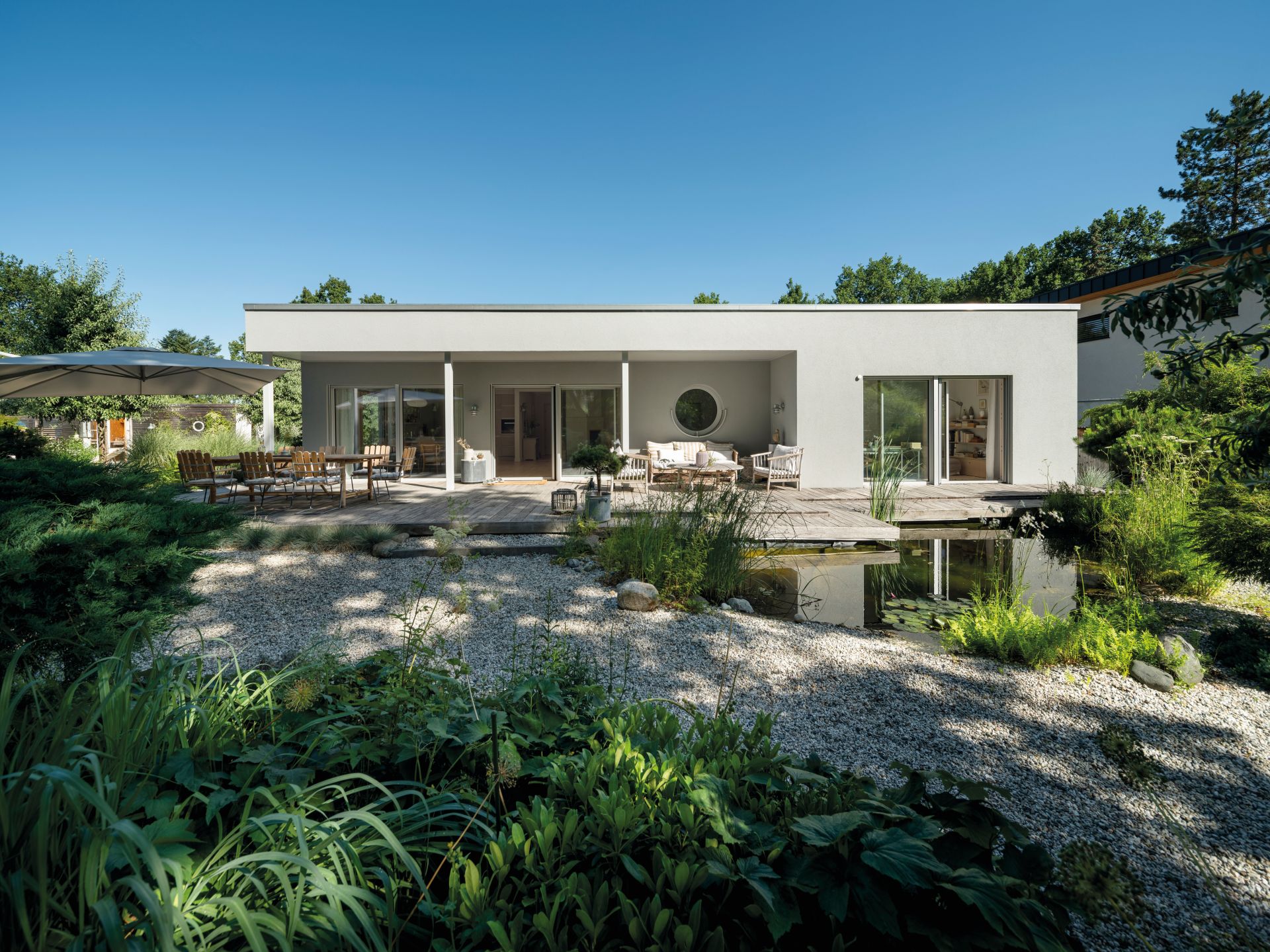 Moderner eingeschossiger Bungalow mit Terrasse, Gartenanlage und bepflanztem Außenbereich.