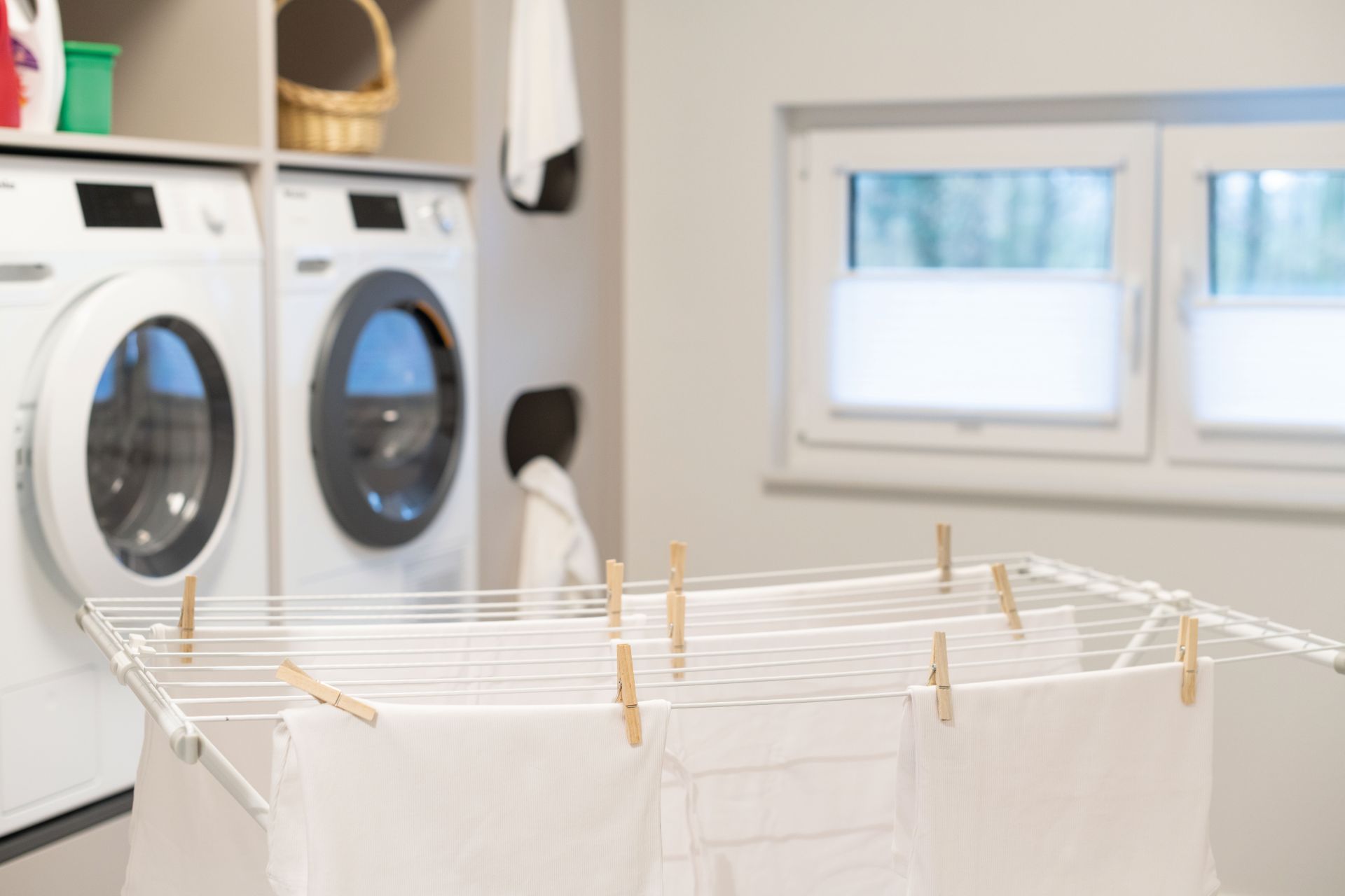 Moderner Hauswirtschaftsraum im FingerHaus Musterhaus SENTO 503 in Bad Vilbel mit Waschmaschine, Trockner und Wäscheständer vor einem Fenster.