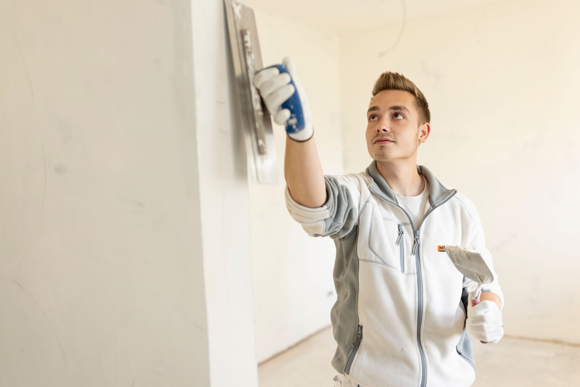 Maler von FingerHaus trägt Innenputz auf eine Wand auf und glättet die Oberfläche sorgfältig im Innenraum eines Hauses.