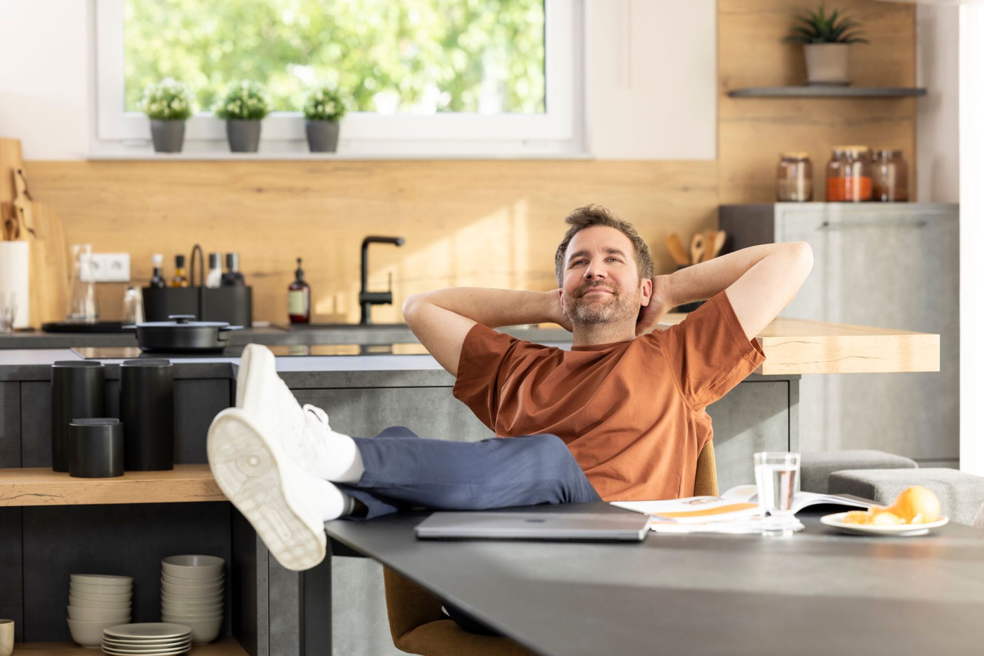 Ein Mann sitzt entspannt am Esstisch eines modernen FingerHaus-Hauses, lehnt sich zurück und genießt die wohnliche Atmosphäre in der Küche.