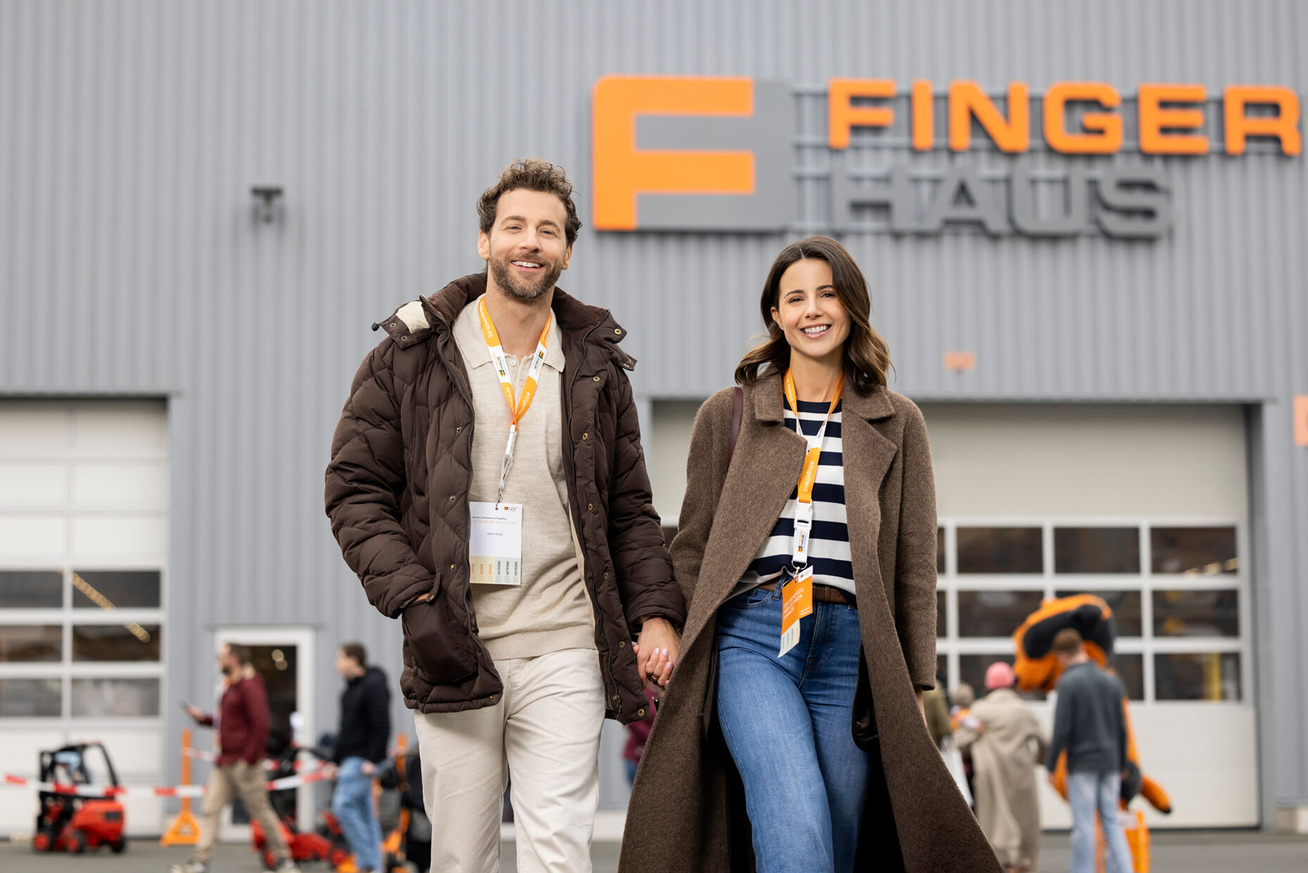 Ein Paar geht lächelnd über das Veranstaltungsgelände des FingerHaus-Bauinfotags in Frankenberg. Im Hintergrund ist eine Halle mit dem FingerHaus-Logo zu sehen, umgeben von weiteren Besuchern.