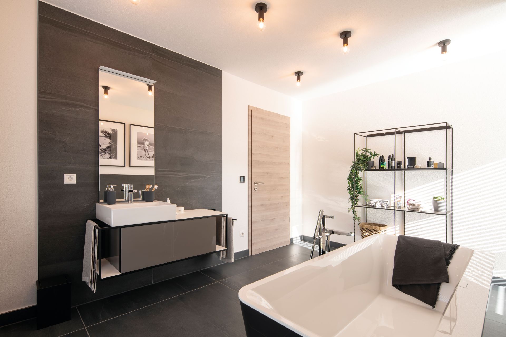 Modernes Badezimmer im Musterhaus MEDLEY 300 B in Frankenberg mit freistehender Badewanne, großem Spiegel und offenem Regal.