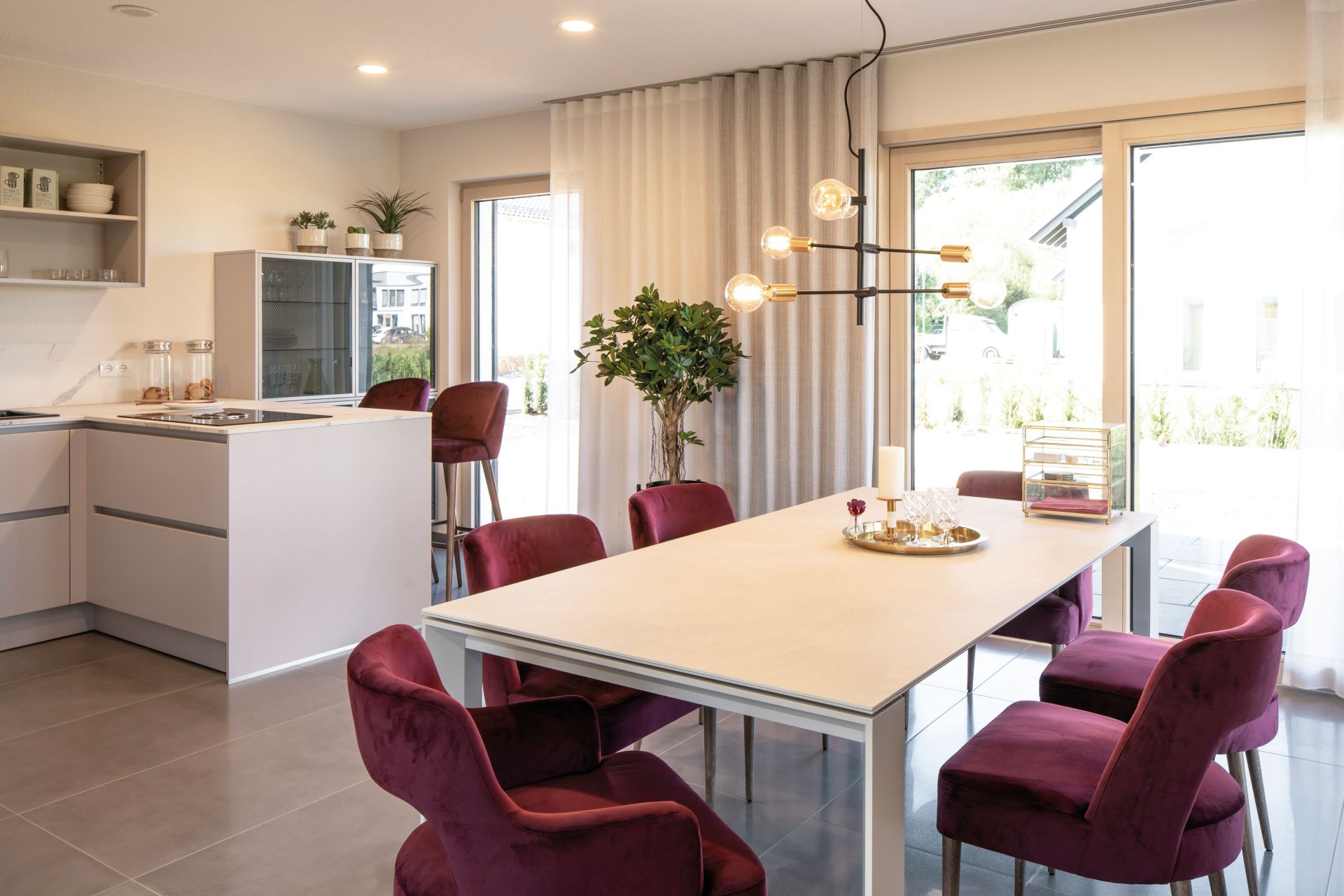 Essbereich im Musterhaus MEDLEY 300 B in Frankenberg mit eleganten weinroten Stühlen, großem Esstisch und moderner offener Küche.
