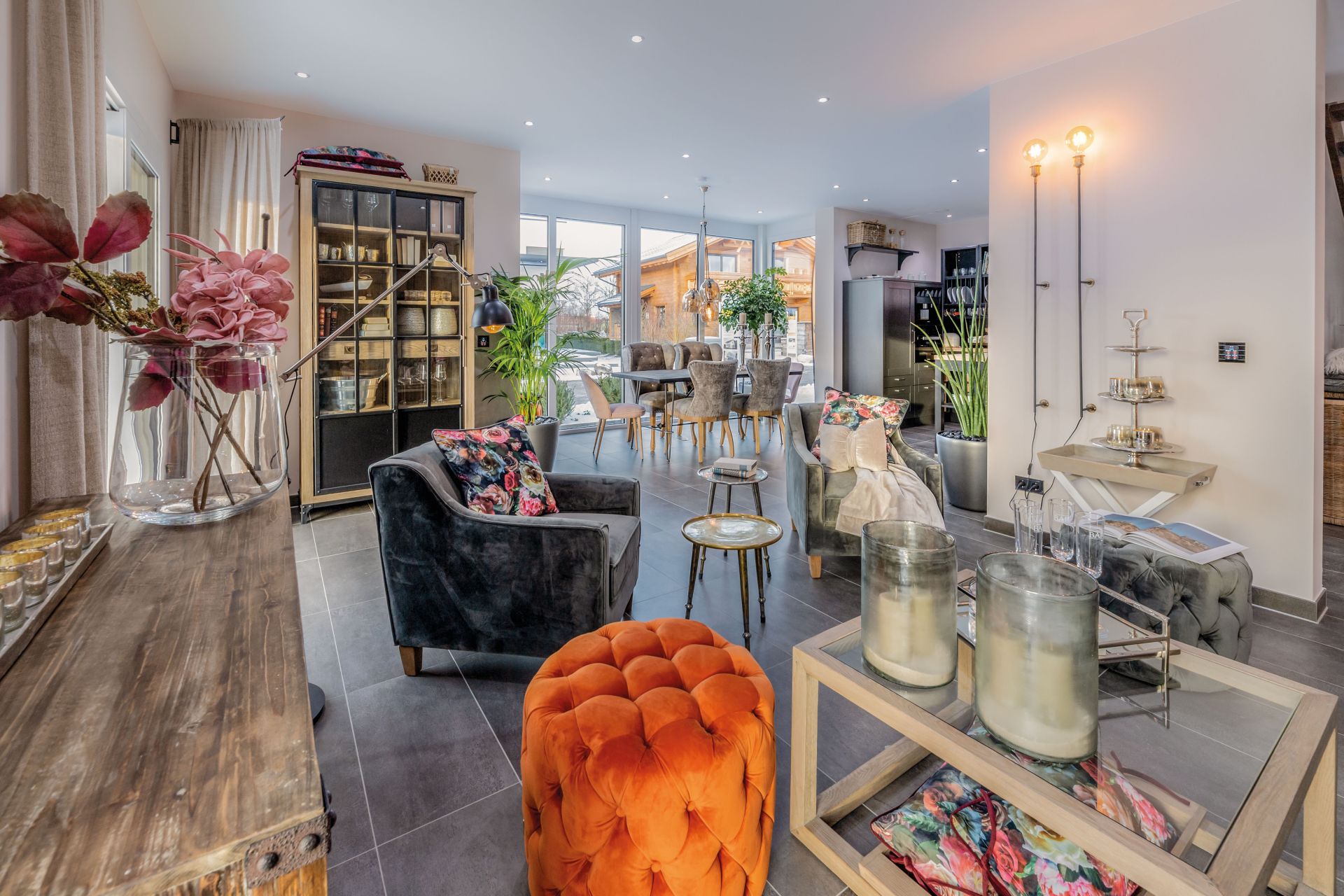 Wohn- und Essbereich im FingerHaus-Musterhaus MEDLEY 3.0 in München mit bunten Polstern, großem Esstisch und viel Tageslicht durch bodentiefe Fenster.