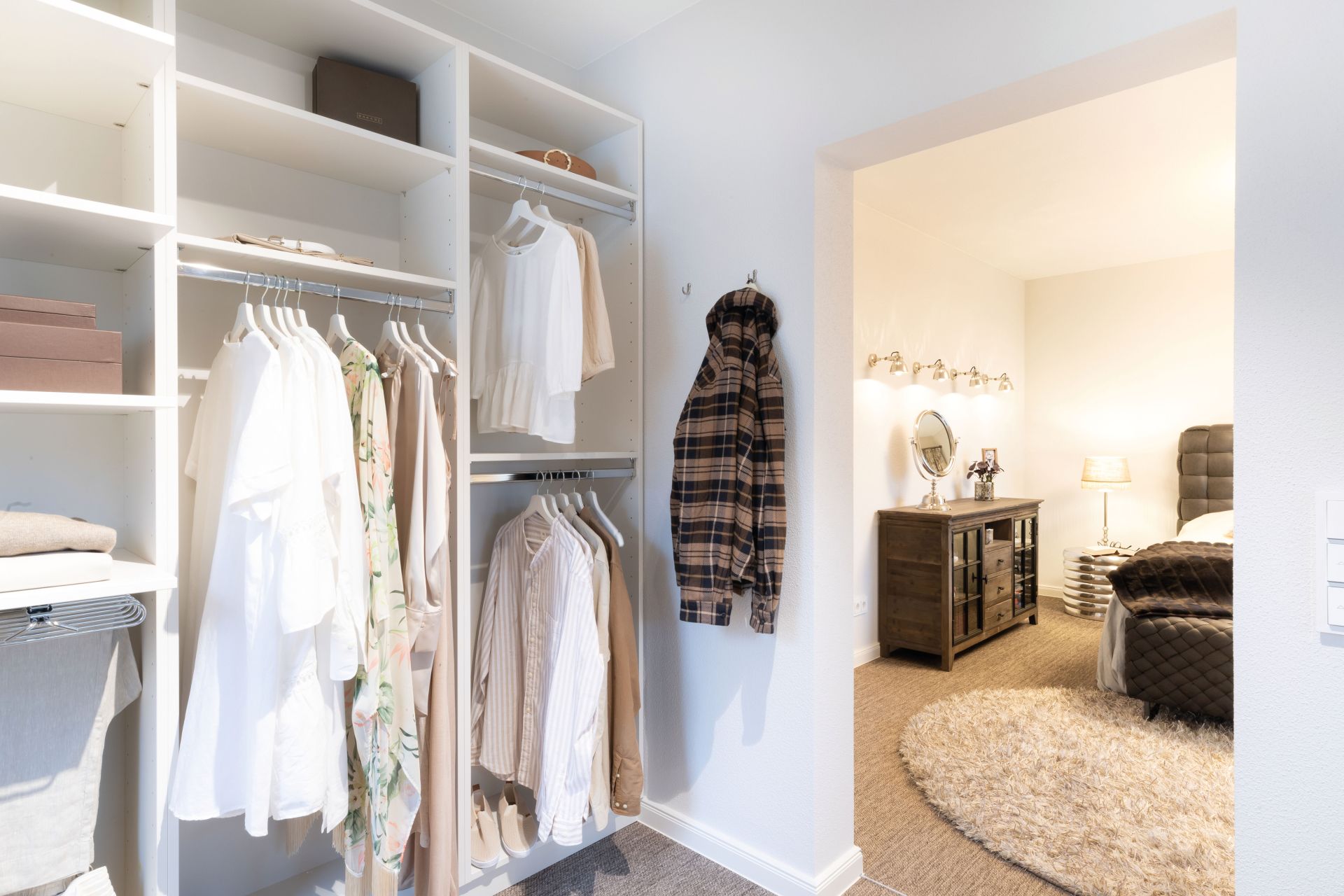 Begehbare Ankleide im Musterhaus SENTO 503 in Bad Vilbel mit offenen Kleiderschränken und direktem Übergang ins Schlafzimmer mit Schminktisch und Doppelbett.
