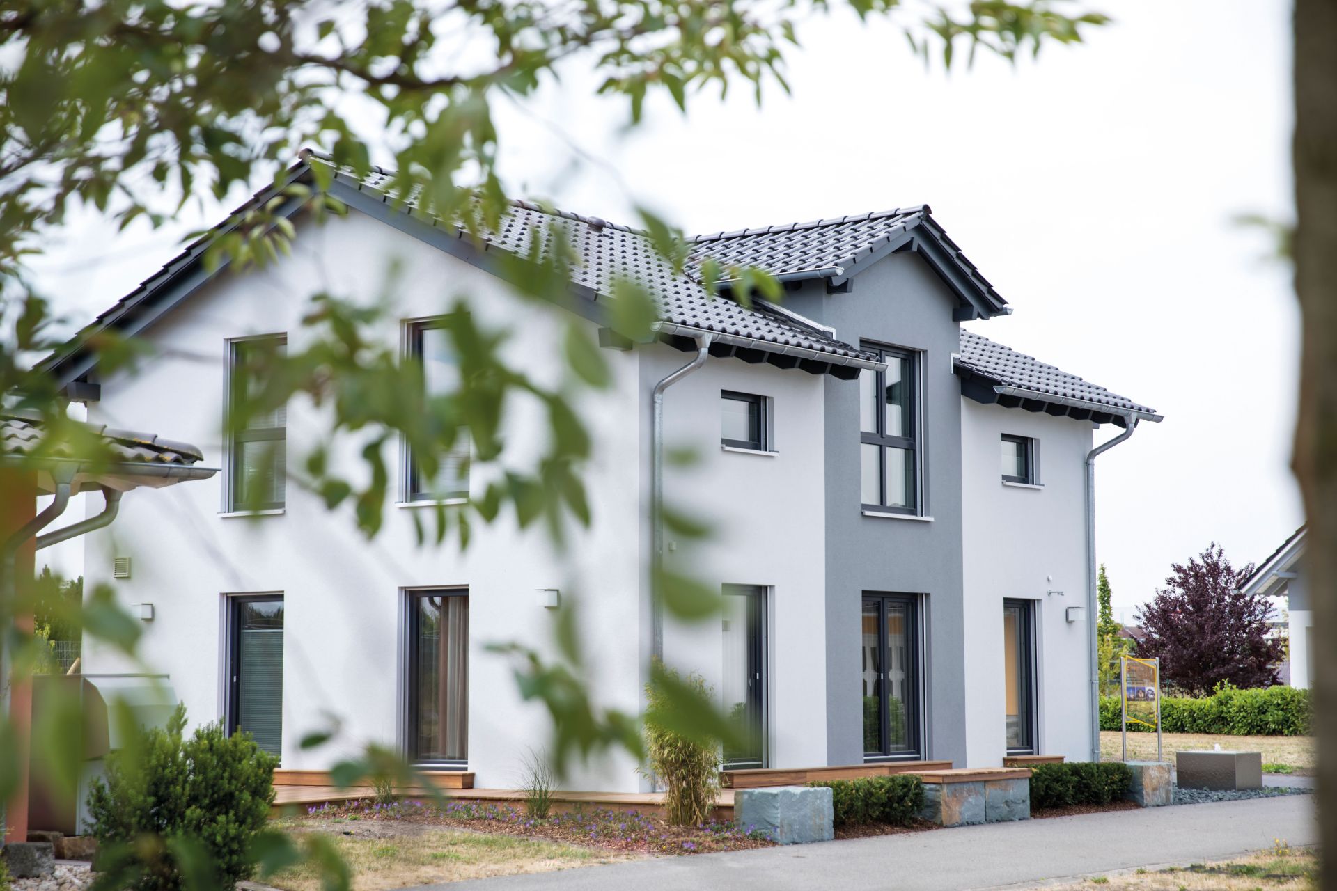 Straßenansicht des Musterhauses UNO 2.0 in Leipzig mit weißer Fassade, grauen Akzenten und Satteldach.