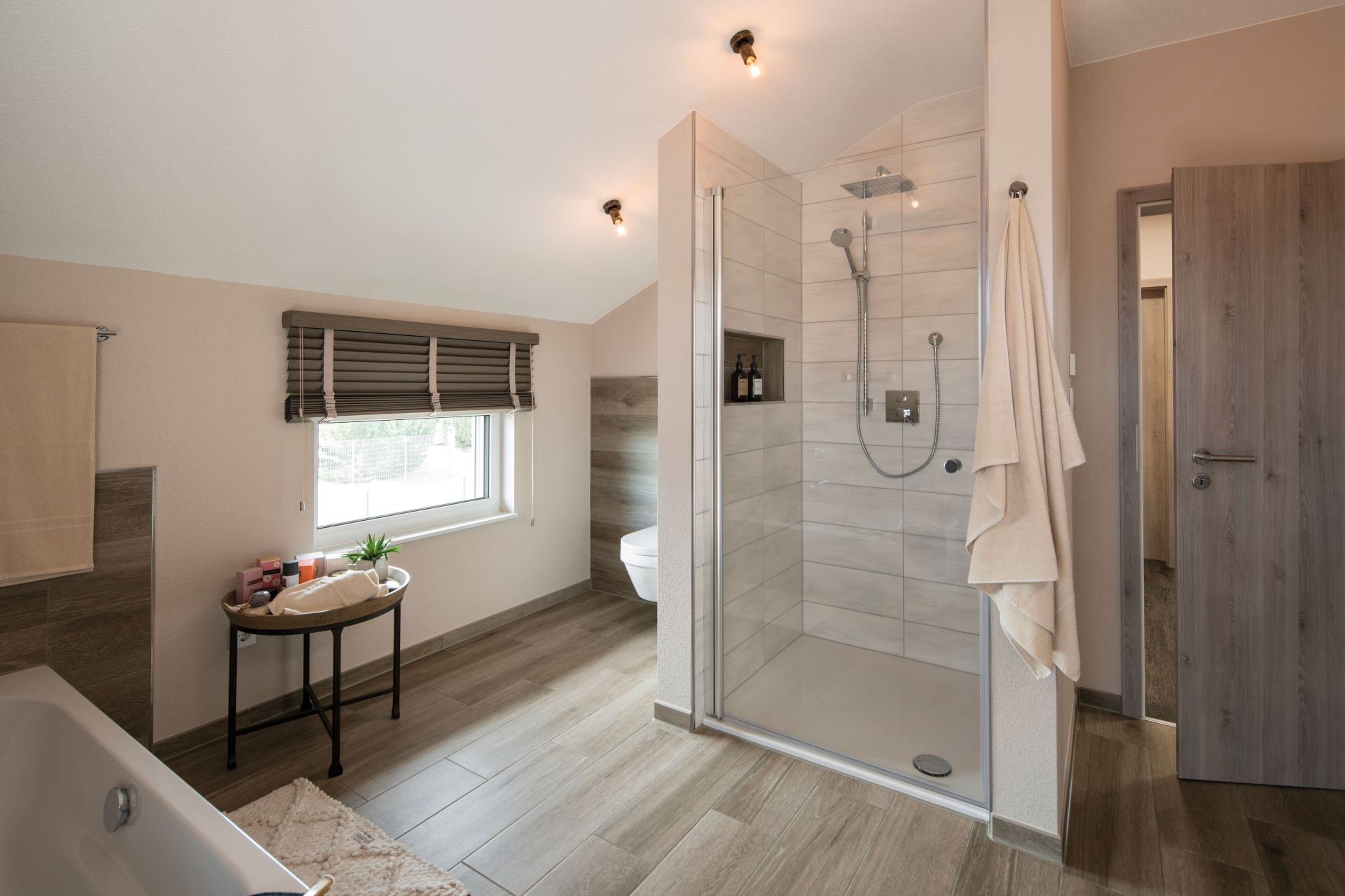 Modernes Badezimmer im Musterhaus UNO 2.0 in Leipzig mit bodengleicher Dusche, Badewanne und Holzoptik-Fliesen.