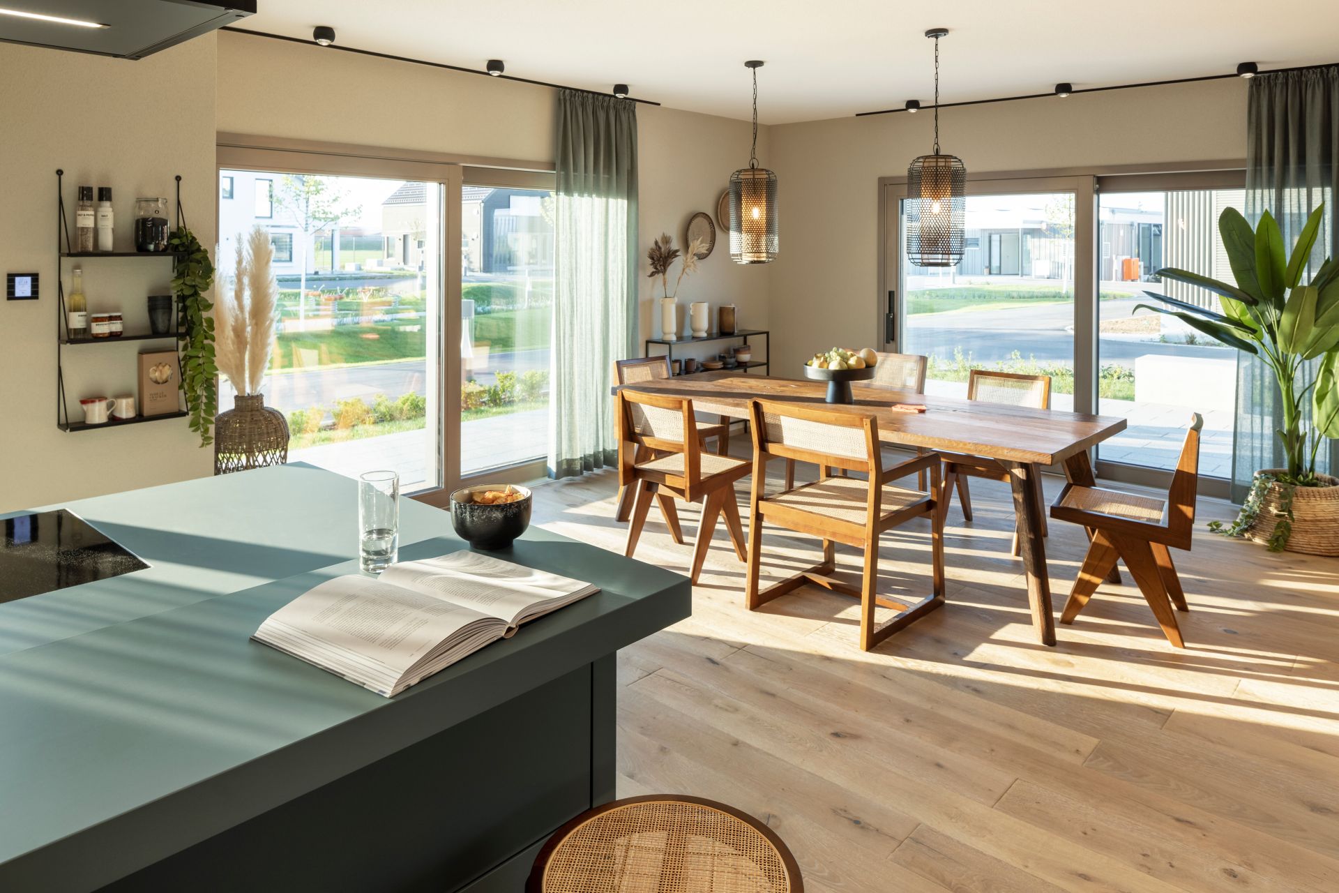 Essbereich im FingerHaus ARTIS 400 Musterhaus Schwarzwald mit großem Holztisch, modernen Stühlen, viel Tageslicht durch große Fensterfronten und offener Küche.