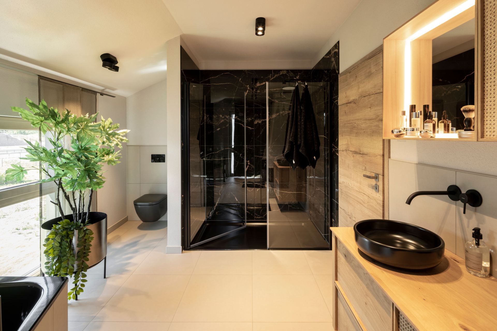 Modernes Badezimmer im FingerHaus ARTIS 300 Musterhaus Nürnberg mit schwarzer Dusche, Aufsatzwaschbecken und stilvoller Holzausstattung.
