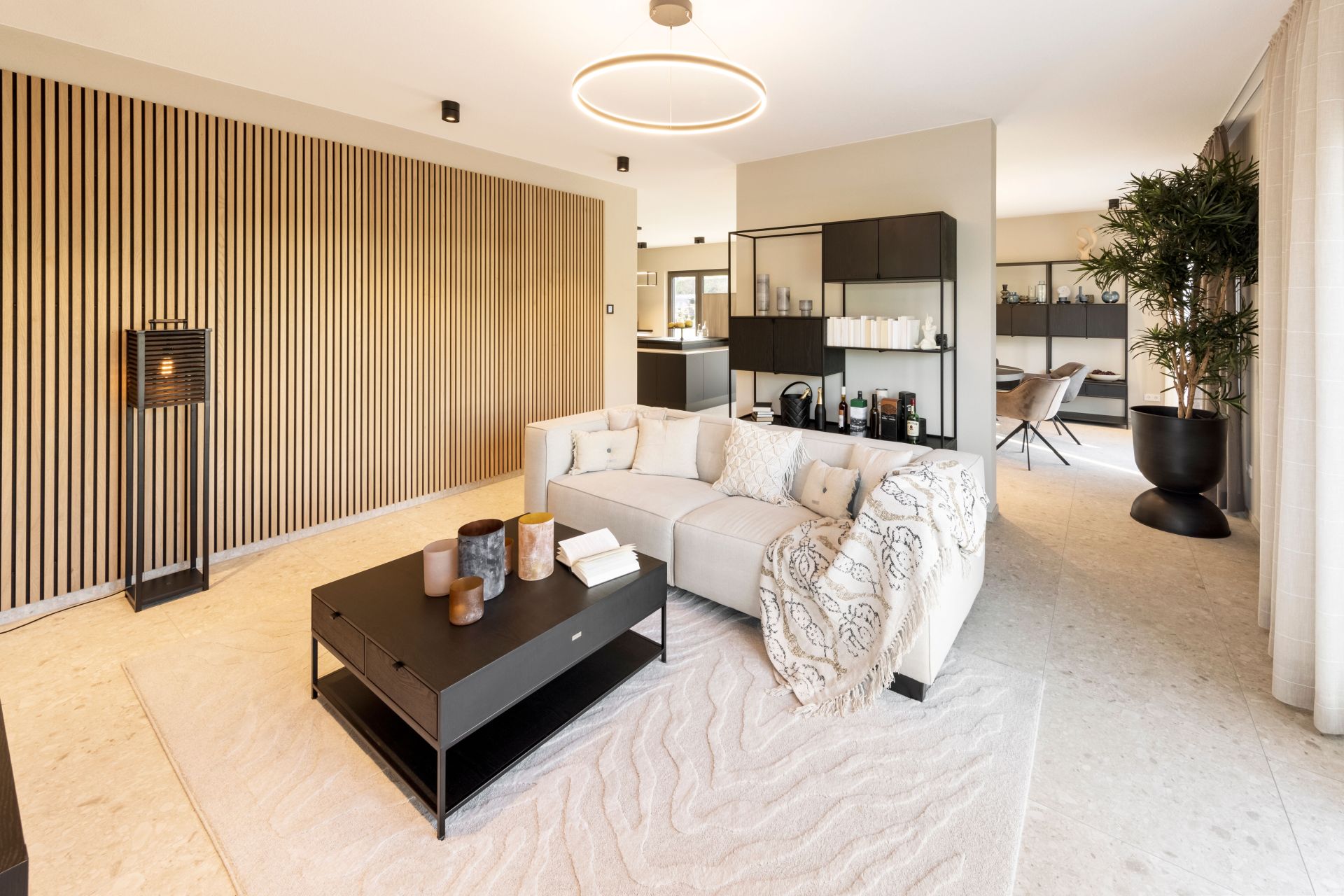 Modernes Wohnzimmer im FingerHaus ARTIS 300 Musterhaus Würzburg mit heller Couch, schwarzem Couchtisch und dekorativer Holzlamellenwand.