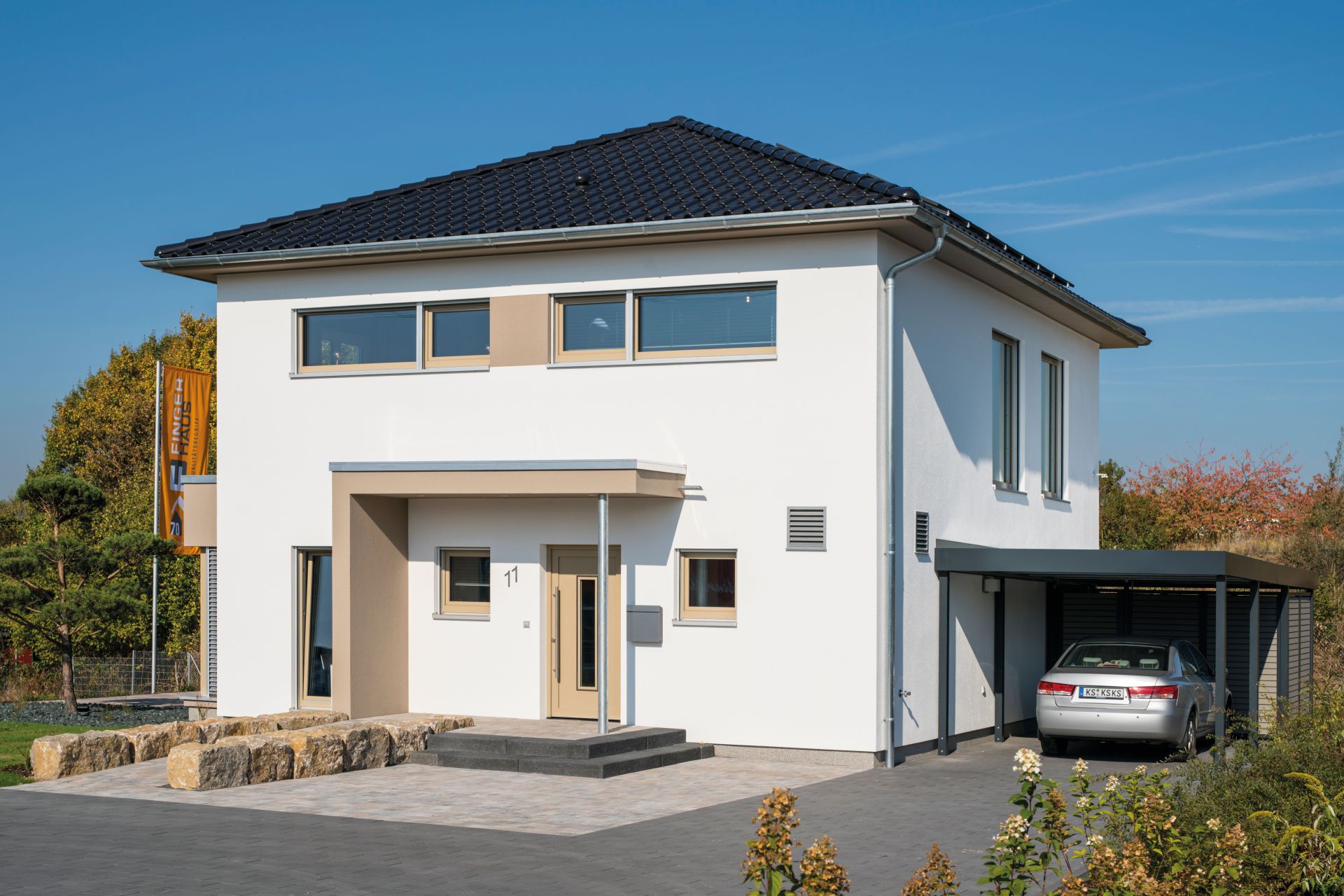 Musterhaus MEDLEY 300 B in Kassel mit Walmdach, modernem Eingangsbereich und angrenzendem Carport mit geparktem Auto.