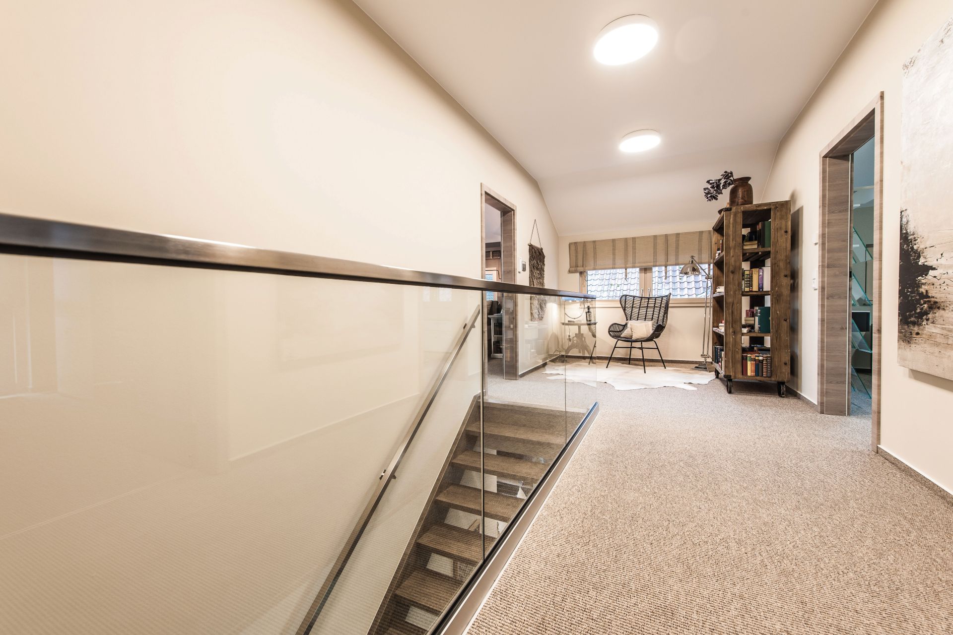 Heller Flurbereich im Obergeschoss des Musterhauses MEDLEY in Fellbach mit Glastreppengeländer, Leseecke und Bücherregal.