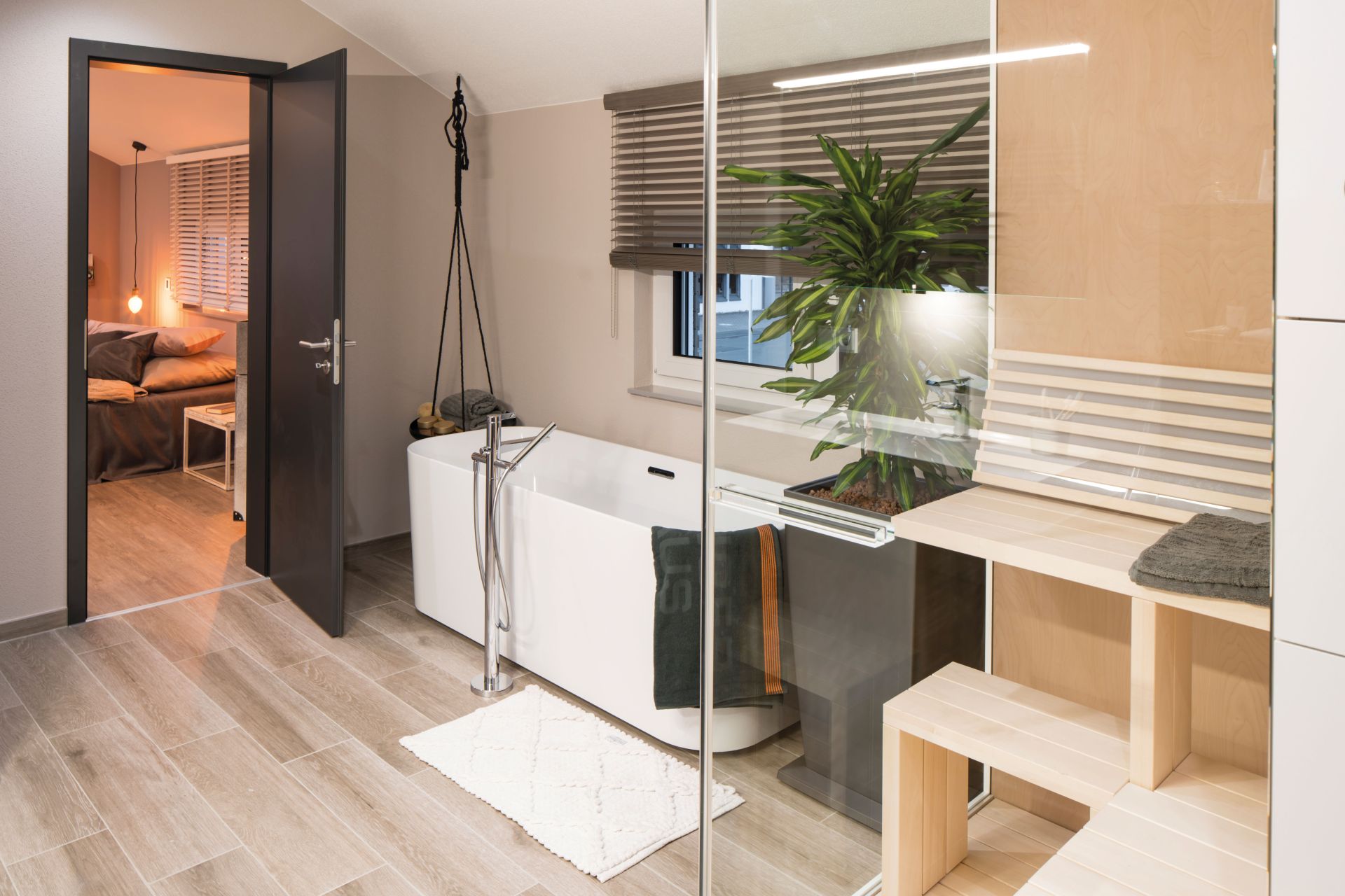 Modernes Badezimmer im FingerHaus SENTO 500 Musterhaus Frankenberg mit freistehender Badewanne, Sauna, Glasabtrennung und Zugang zum Schlafzimmer.