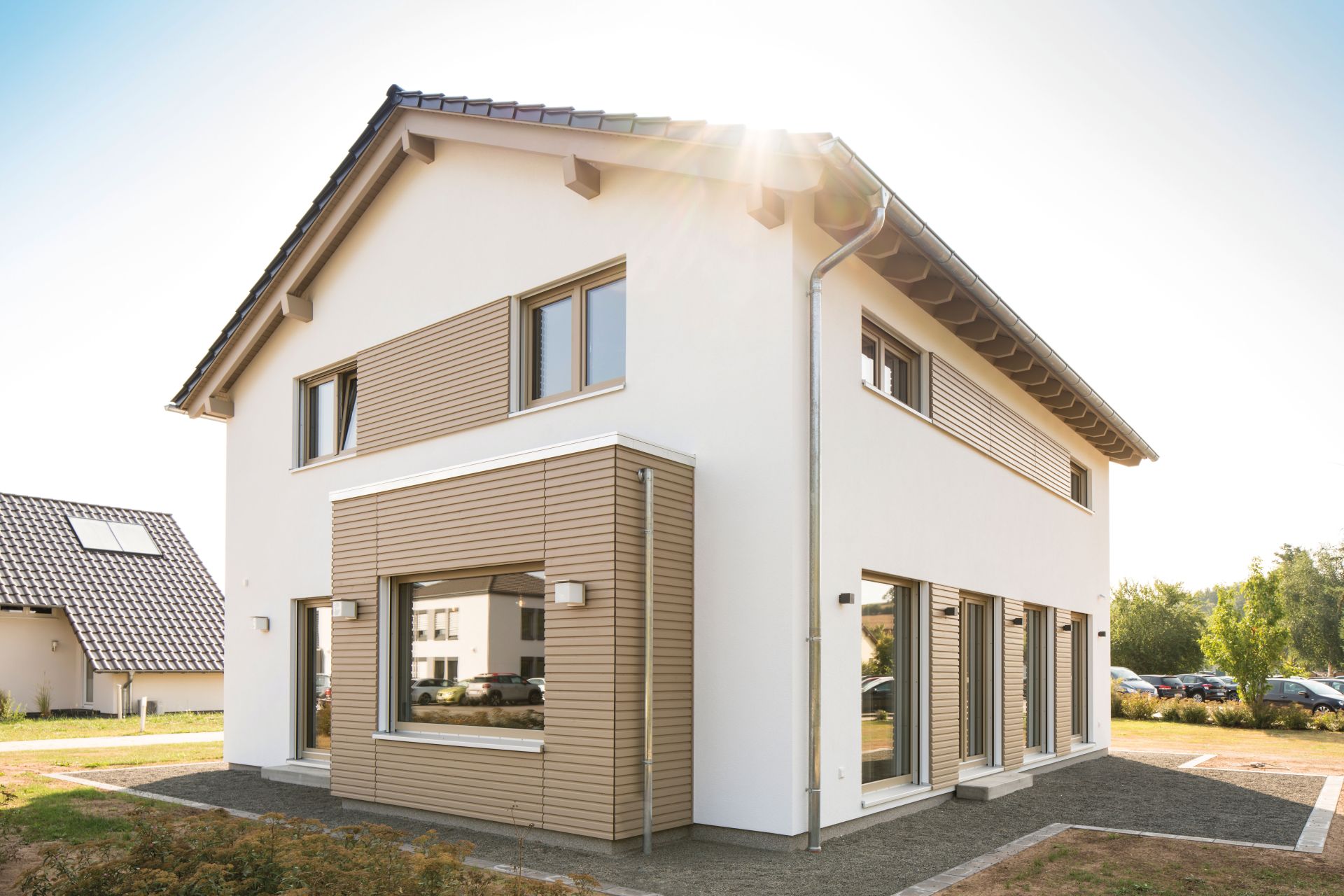 FingerHaus SENTO 500 Musterhaus in Frankenberg mit Satteldach, weißer Fassade und modernen Holz-Elementen an den Fensterbereichen, aufgenommen bei Sonnenschein.