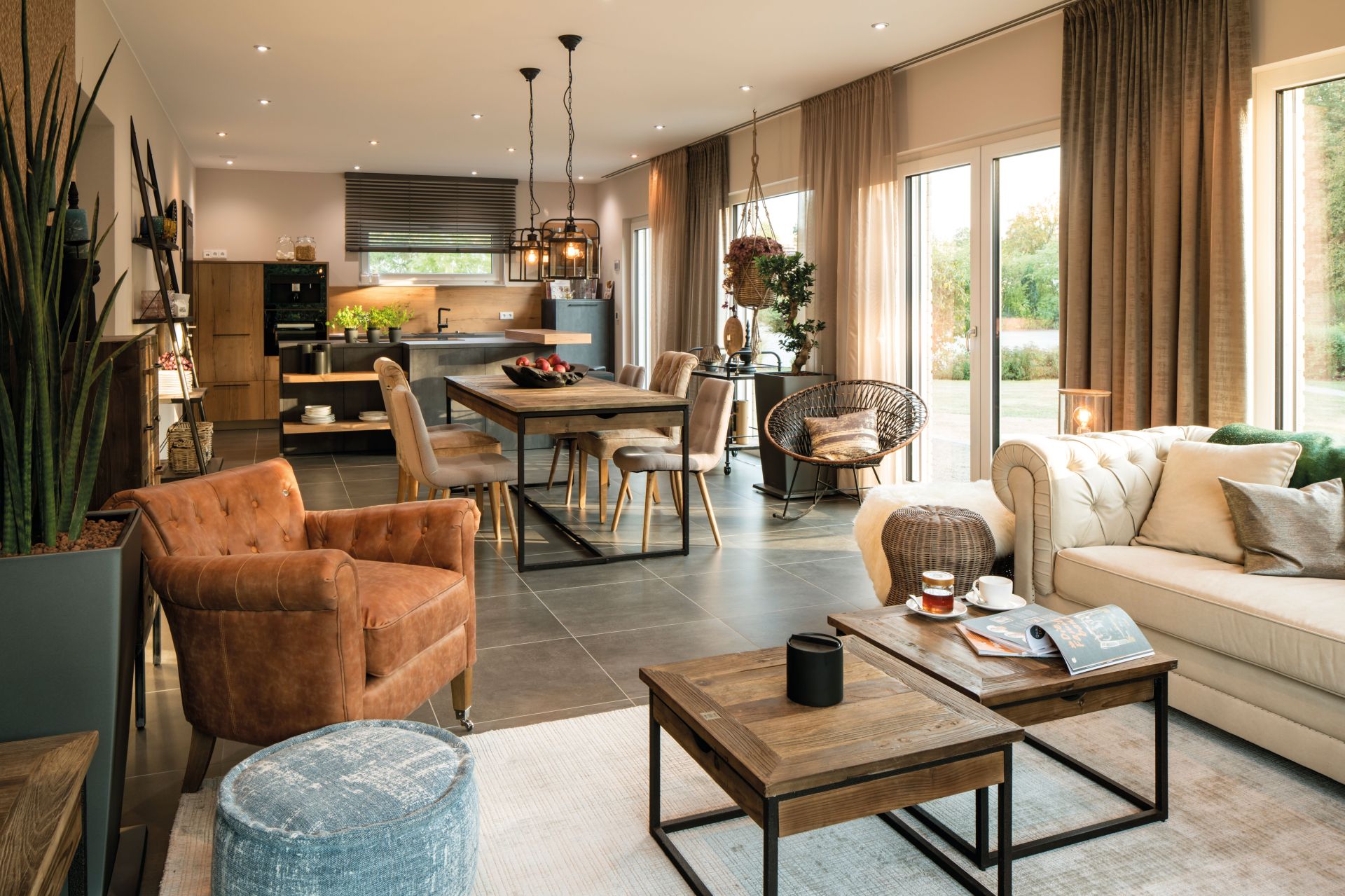 Modern eingerichtetes Wohnzimmer im FingerHaus SENTO 500 Musterhaus in Frankenberg mit hellen Sofas, rustikalem Esstisch, offener Küche und großen Fenstern.