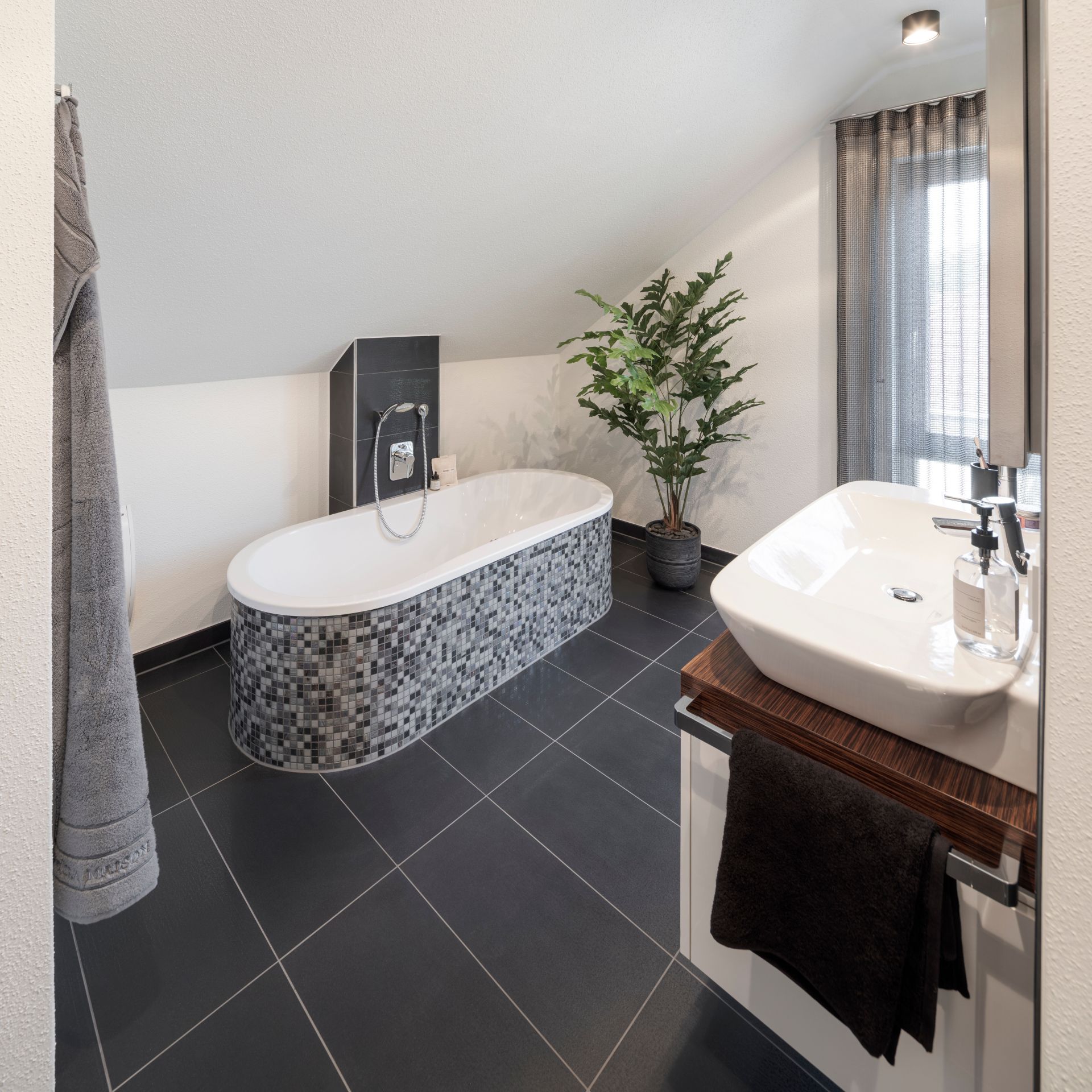 Modernes Badezimmer im frei geplanten FingerHaus Musterhaus Marburg mit Badewanne in Mosaikoptik und Waschtisch.