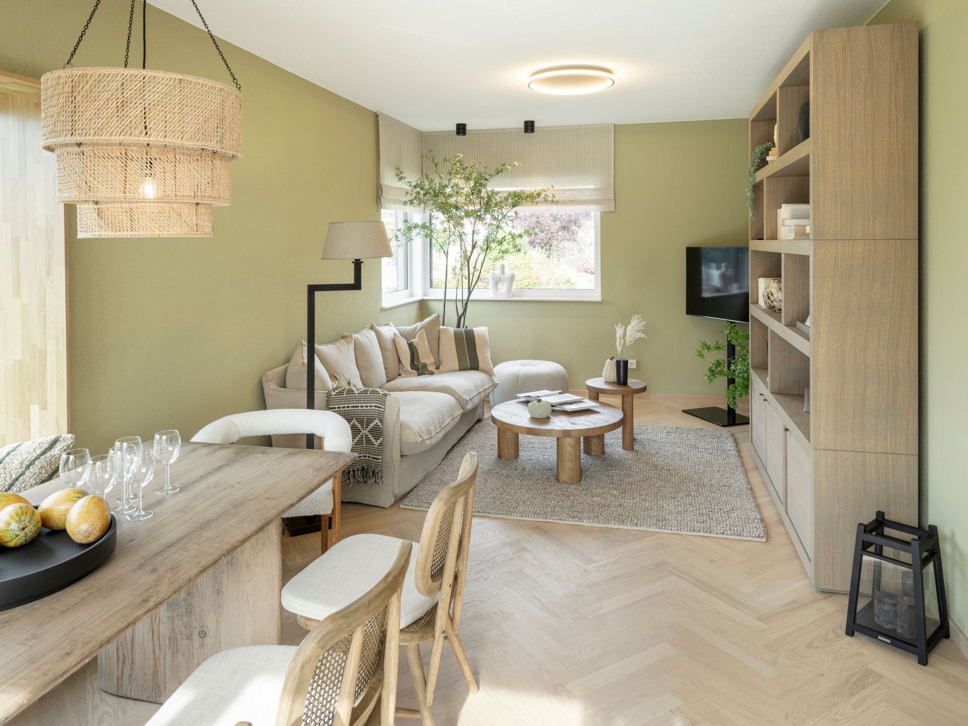 Helles Wohnzimmer im Musterhaus JUNO 300 in Mülheim-Kärlich mit Sofa, Holztisch, Bücherregal und großen Fenstern.