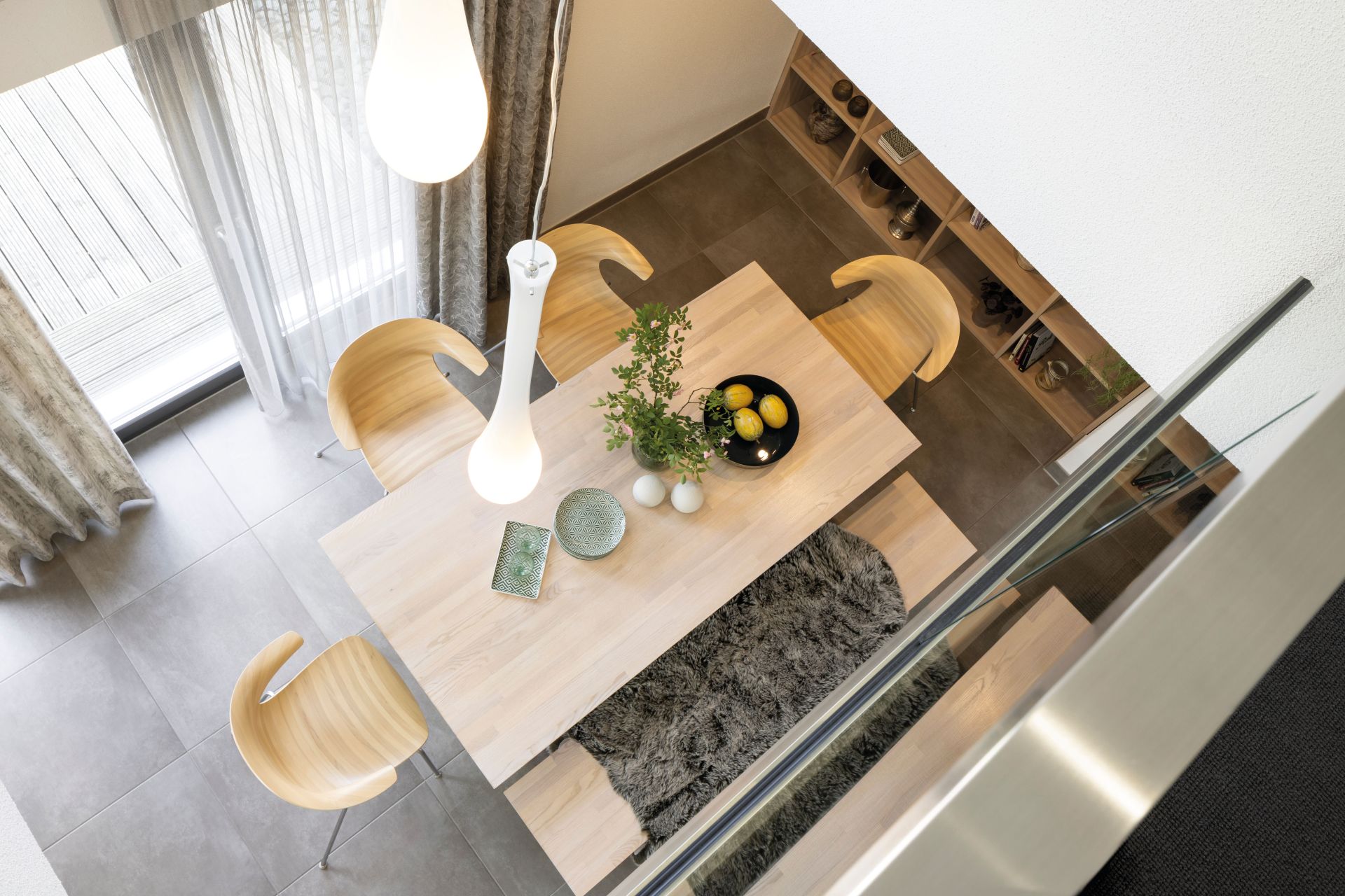 Blick von oben auf den Essbereich mit Holztisch, modernen Stühlen und dekorativen Hängelampen im Musterhaus NEO 300 in Hannover.