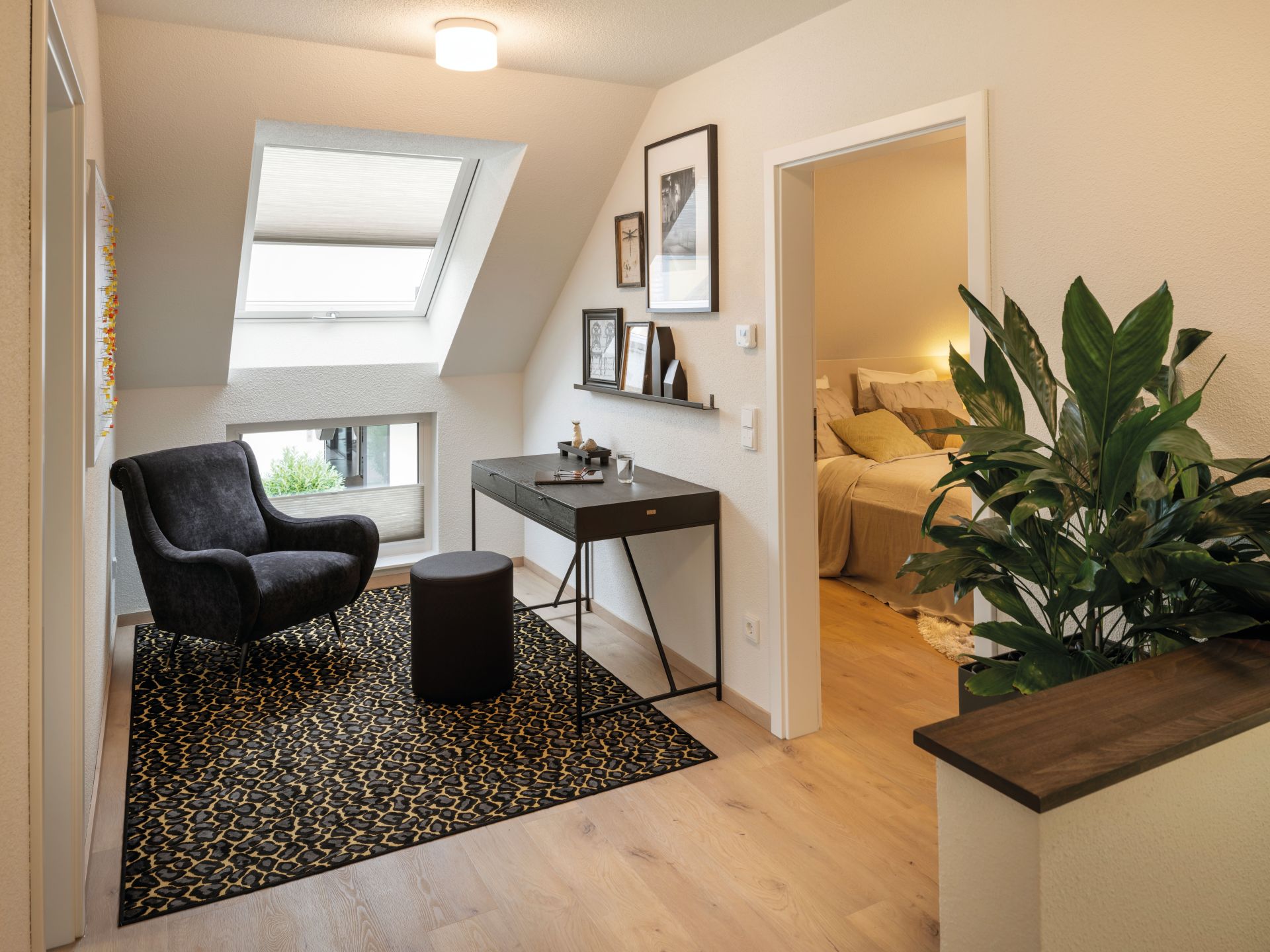 Gemütlicher Arbeits- und Loungebereich im Obergeschoss des Musterhauses NEO in Wuppertal mit Sessel, Schreibtisch und Dachfenster.
