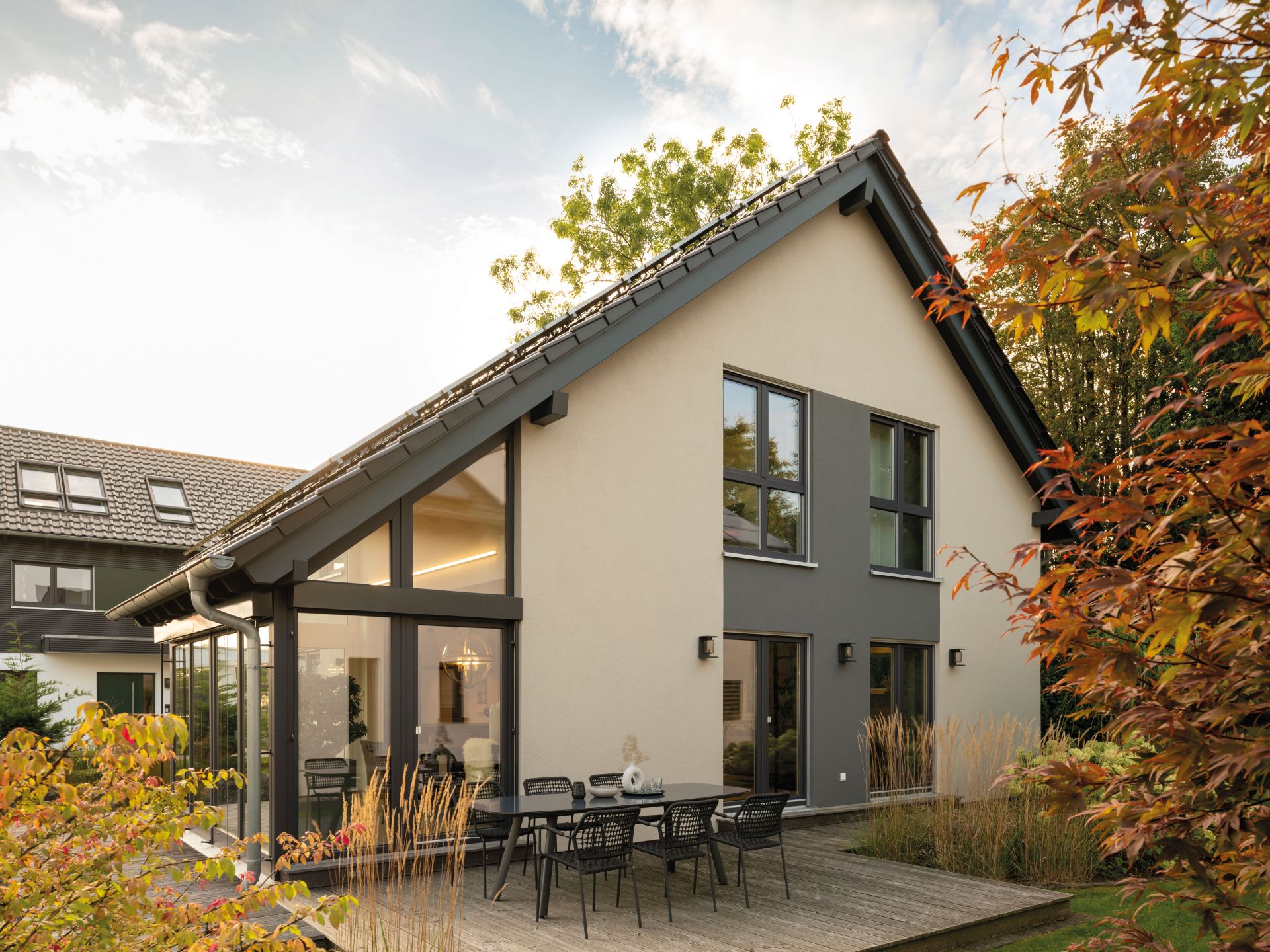 Musterhaus NEO in Wuppertal mit moderner Fassade, großflächigen Fenstern, Holzterrasse und gemütlichem Essplatz im Freien.