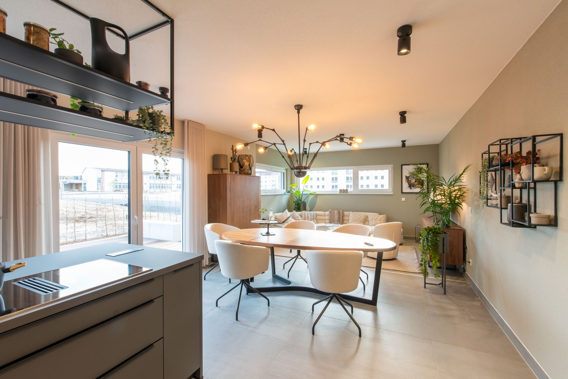 Moderner Essbereich im FingerHaus Musterhaus TALO in Babenhausen mit großem Esstisch, eleganten weißen Stühlen und auffälliger Designerleuchte. Offenes Wohnkonzept mit angrenzender Küche und stilvollen Deko-Elementen.