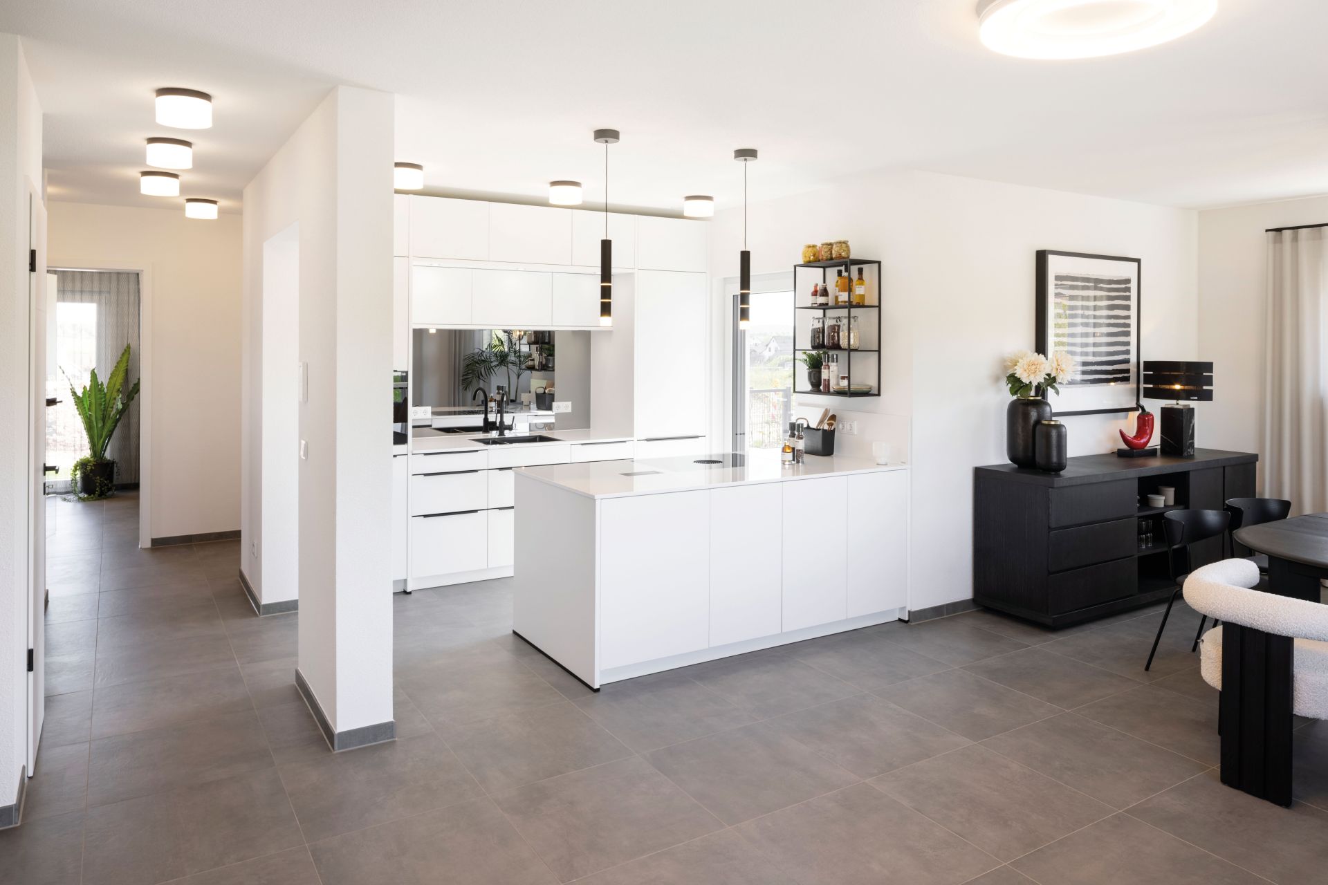 Moderne offene Küche im Musterhaus TALO Fulda mit Kochinsel, weißen Fronten und Essbereich.