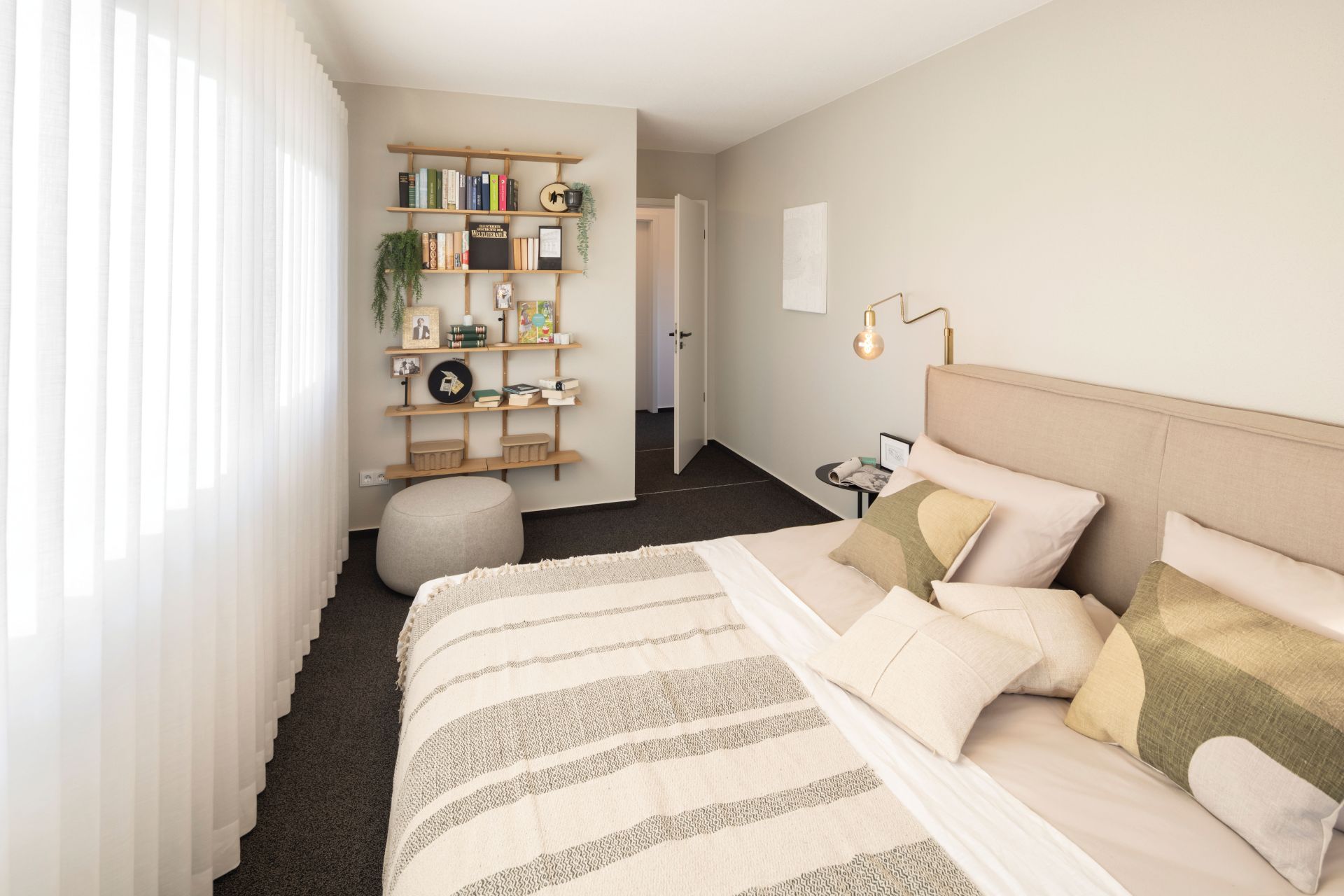 Helles Schlafzimmer im Musterhaus TALO Fulda mit gemütlichem Bett, Bücherregal und modernem Einrichtungsstil.