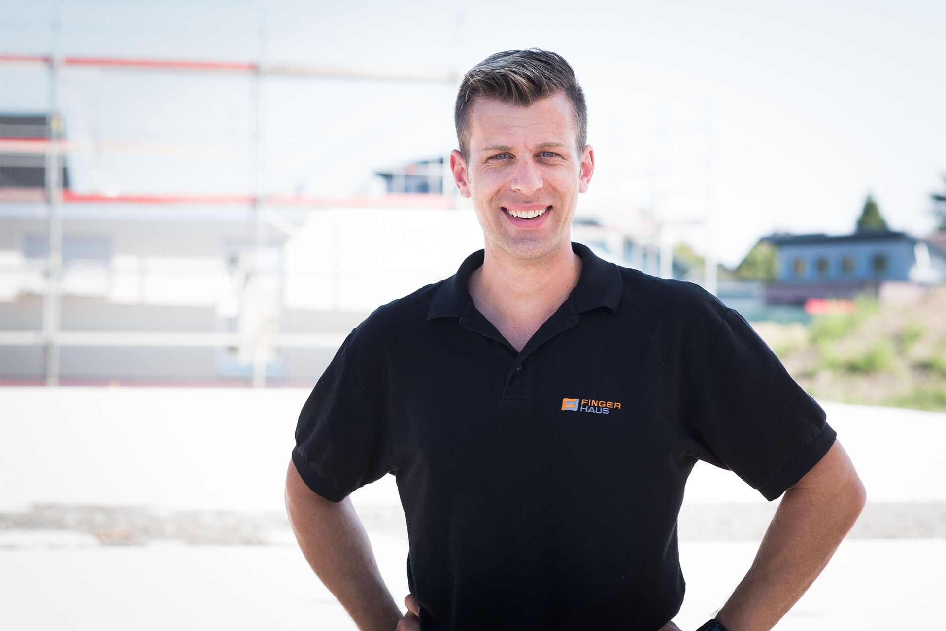 Mitarbeiter von FingerHaus steht lächelnd auf einer Baustelle, Arbeitsumfeld im Hintergrund, Karriere bei FingerHaus.