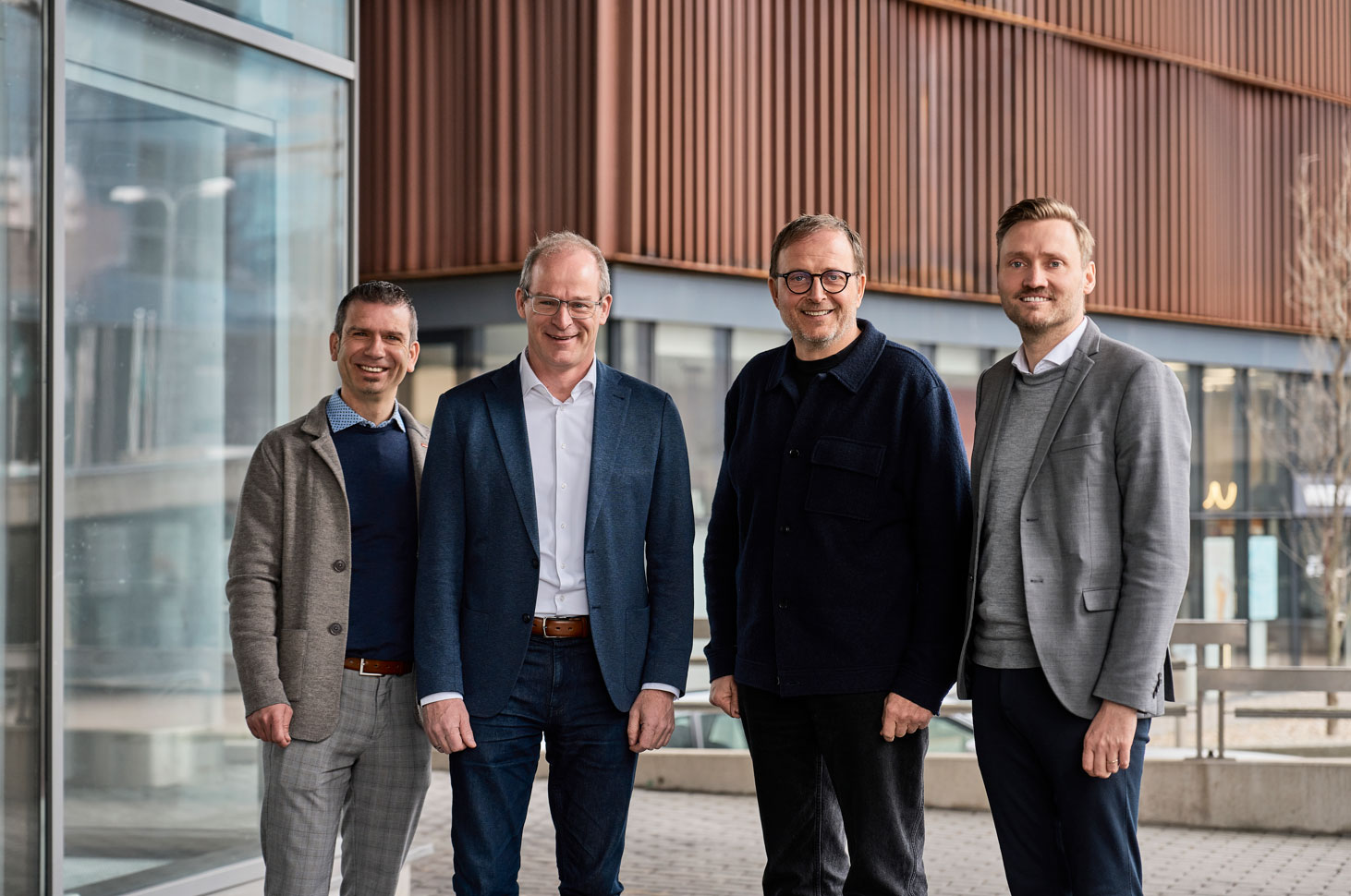 Vier Personen stehen vor einem modernen Bürogebäude mit Glasfassade und Holzlamellenfassade. Von links nach rechts: Jan Wegner (VELUX), Dr. Mathias Schäfer und Klaus Cronau (FingerHaus Geschäftsführung) sowie André Osterhoff (VELUX).